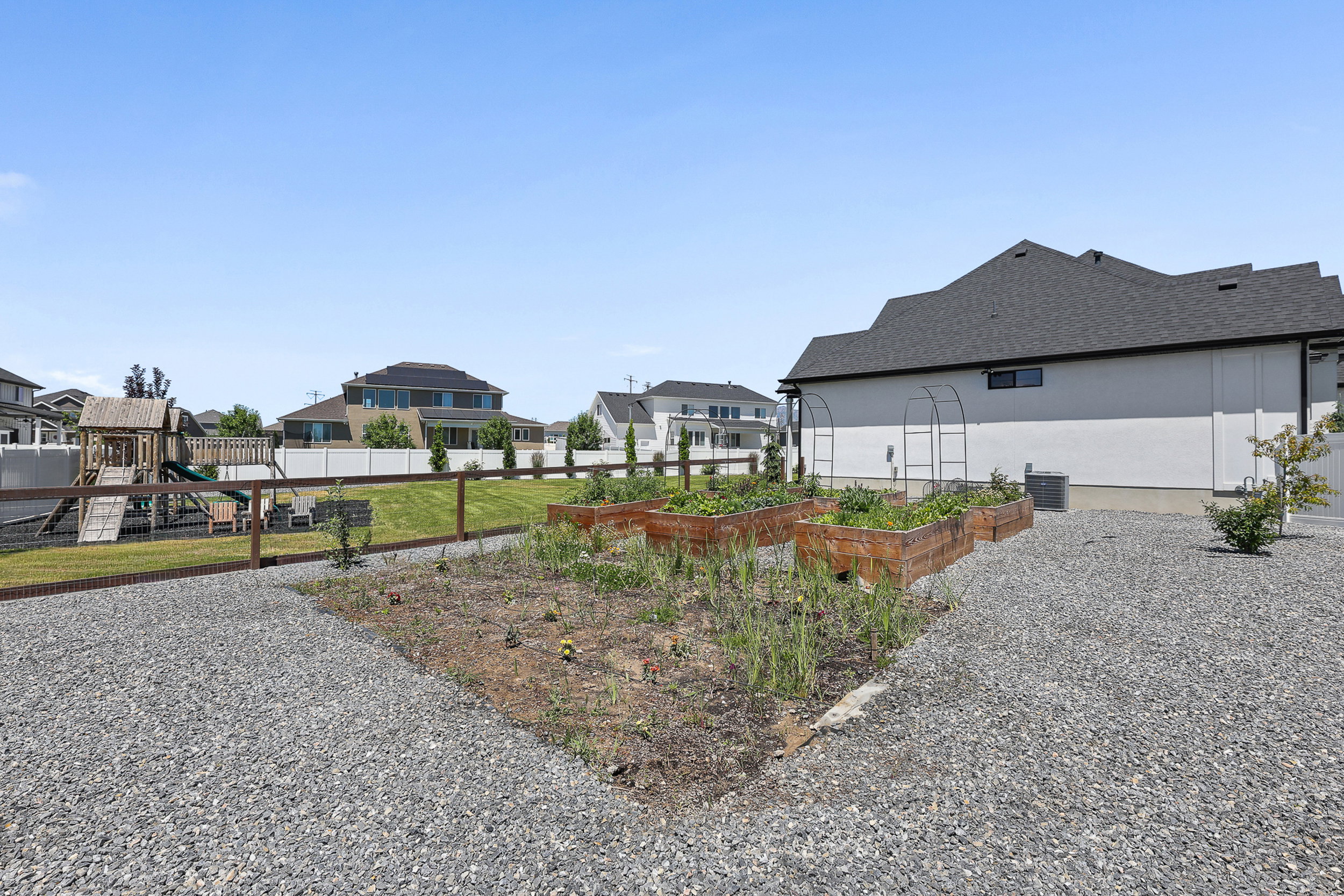Expansive outdoor space featuring multiple raised garden beds, a dedicated gravel area, and a wooden play structure