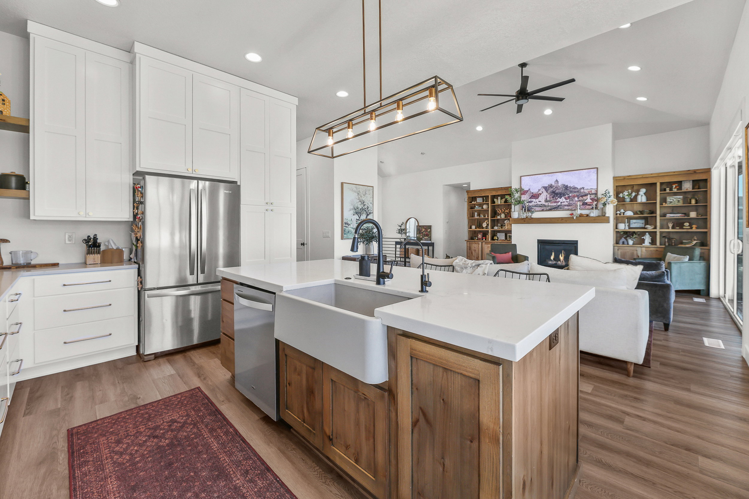 Open-concept kitchen featuring an island with a farmhouse sink and white countertops, stainless steel appliances, white cabinetry, and wood-finish flooring
