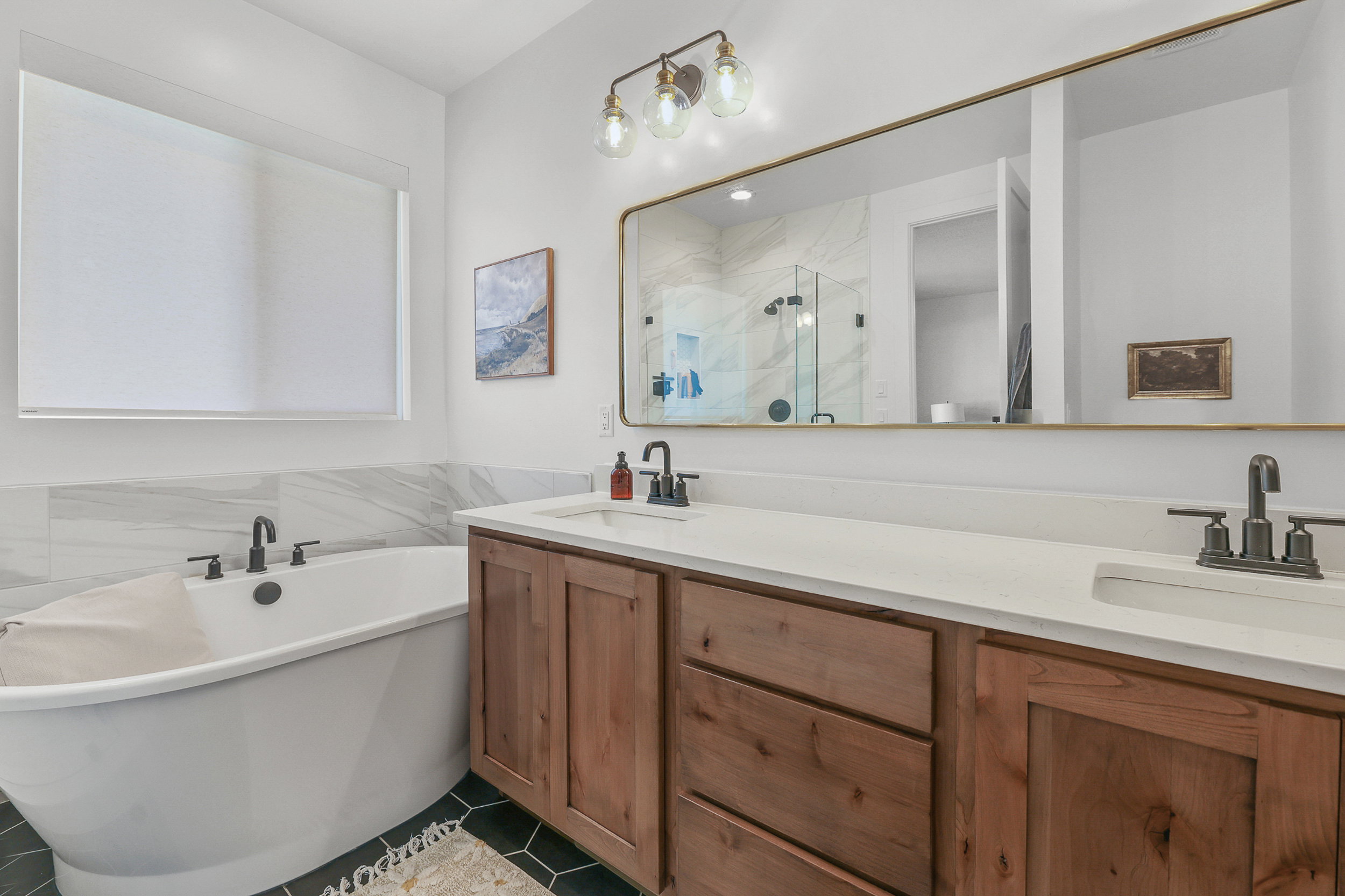 Bathroom featuring a freestanding soaking tub, dual vanity with wood-finish cabinetry, white countertops, and a large frameless mirror