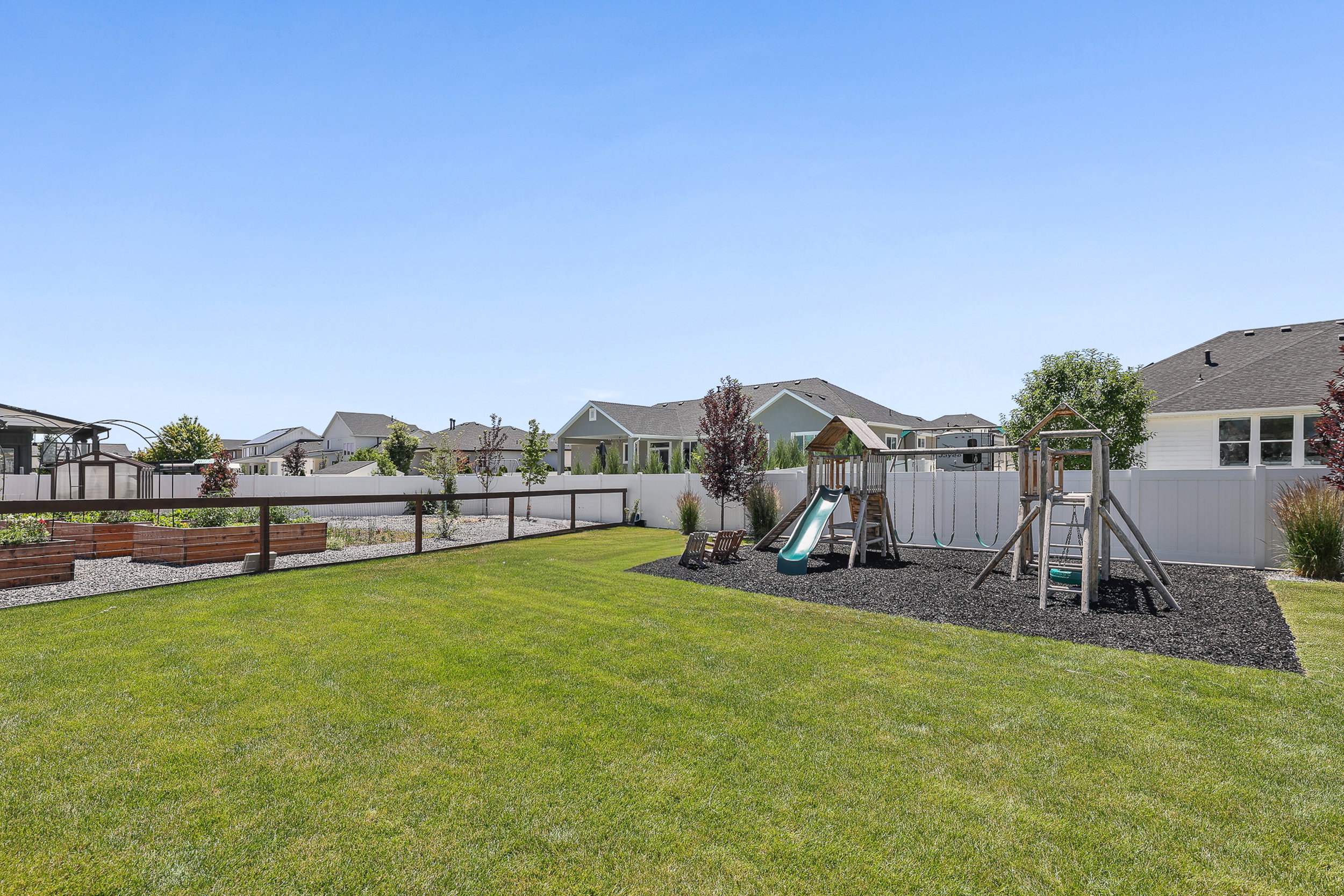 Expansive backyard featuring a manicured lawn, dedicated play area with soft ground cover, and raised garden beds