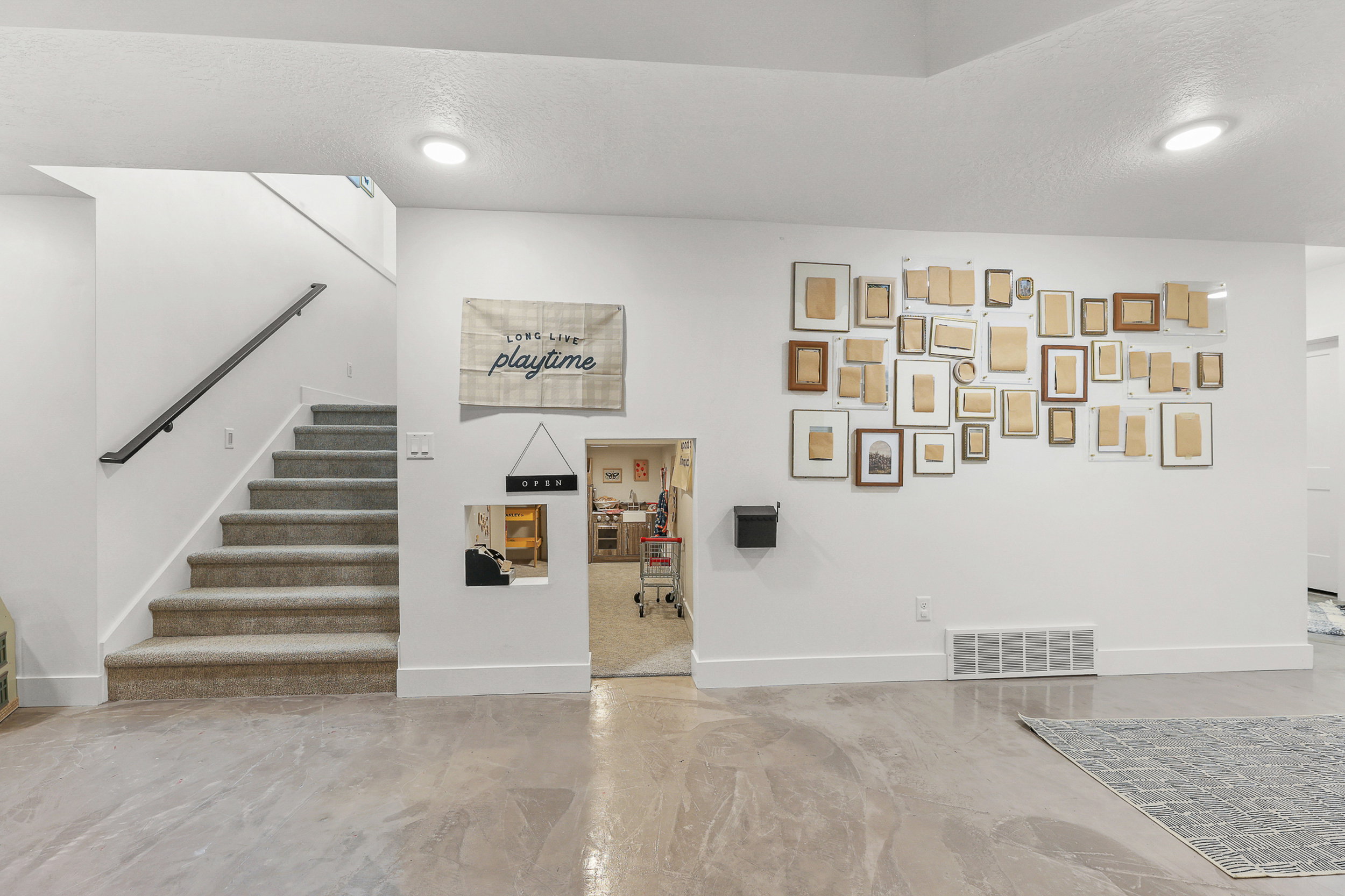 Finished basement space featuring concrete-finish flooring, a carpeted staircase with a dark handrail, and recessed ceiling lighting