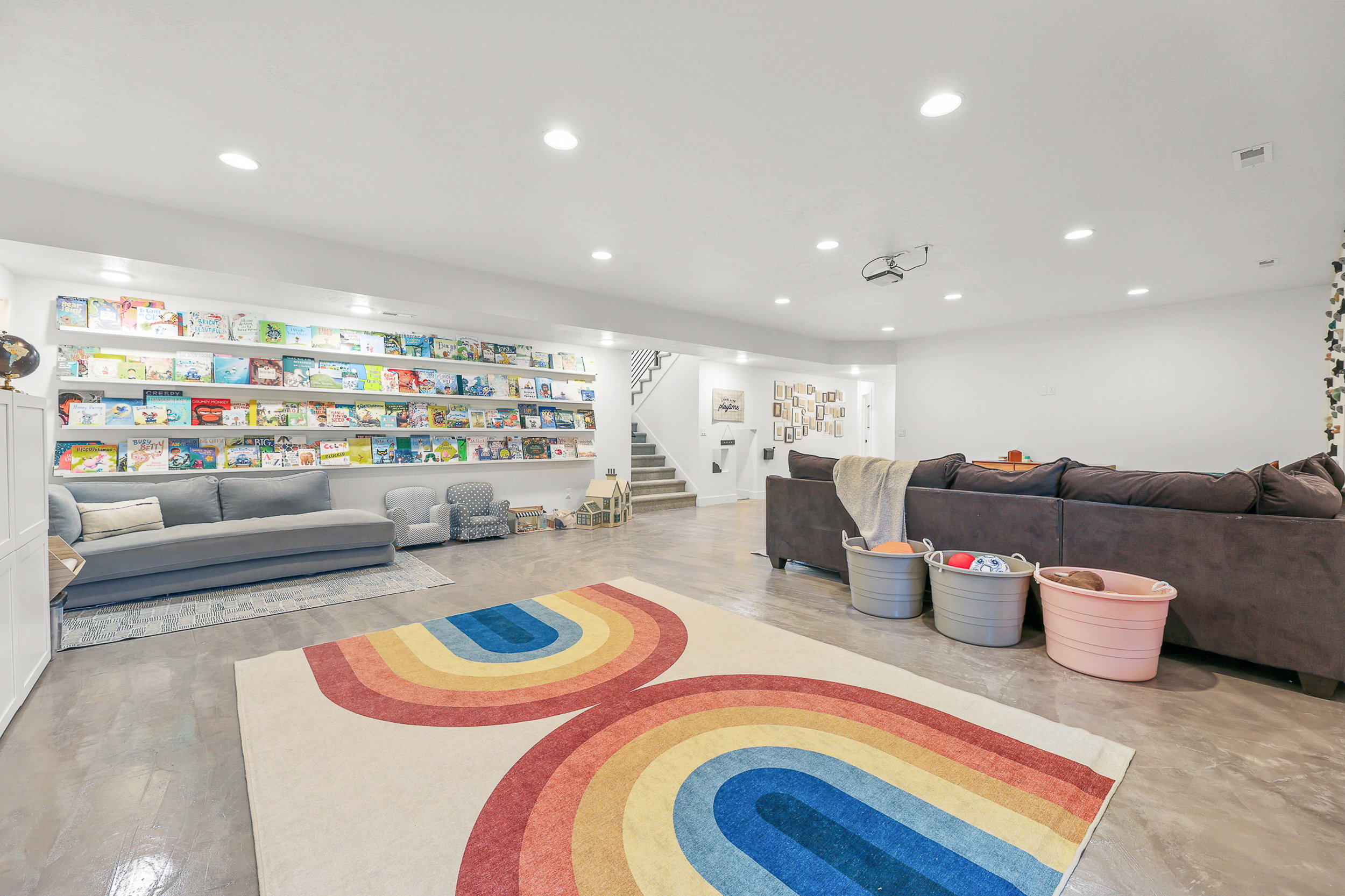 Spacious lower-level area featuring recessed lighting, a built-in projector, and a full wall of floating shelves