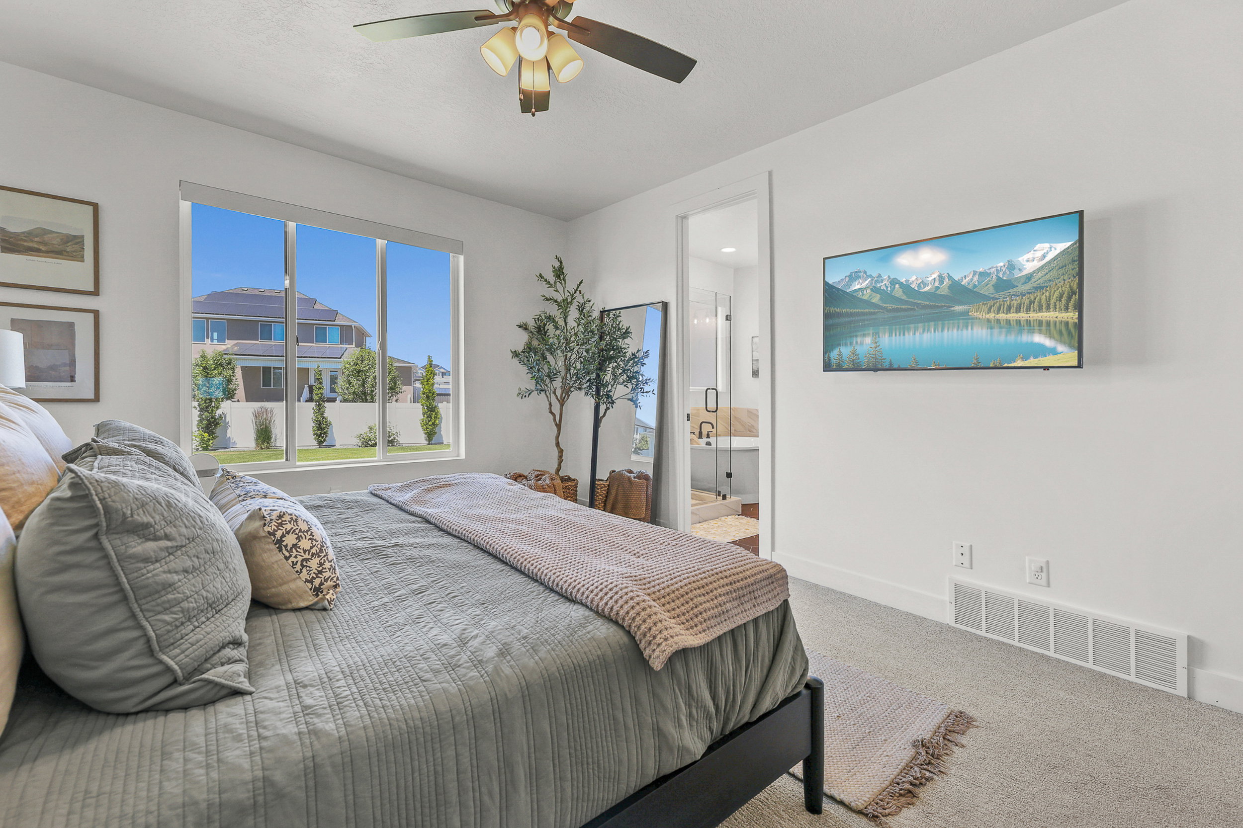 Carpeted bedroom with a ceiling fan, large window, and wall-mounted television