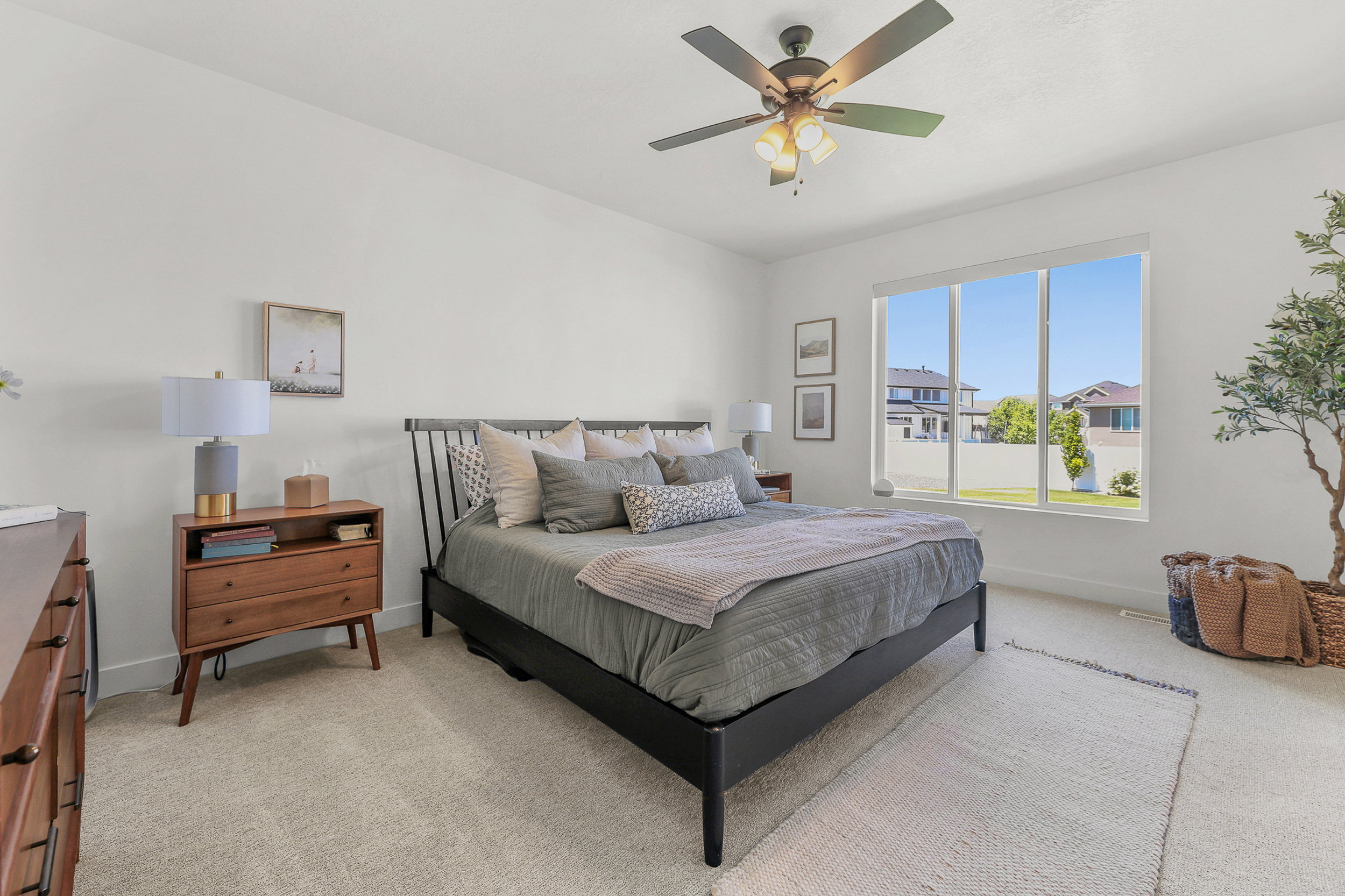 Expansive bedroom featuring white walls, light-toned carpet flooring, a large window offering natural light, and a ceiling fan with integrated lighting