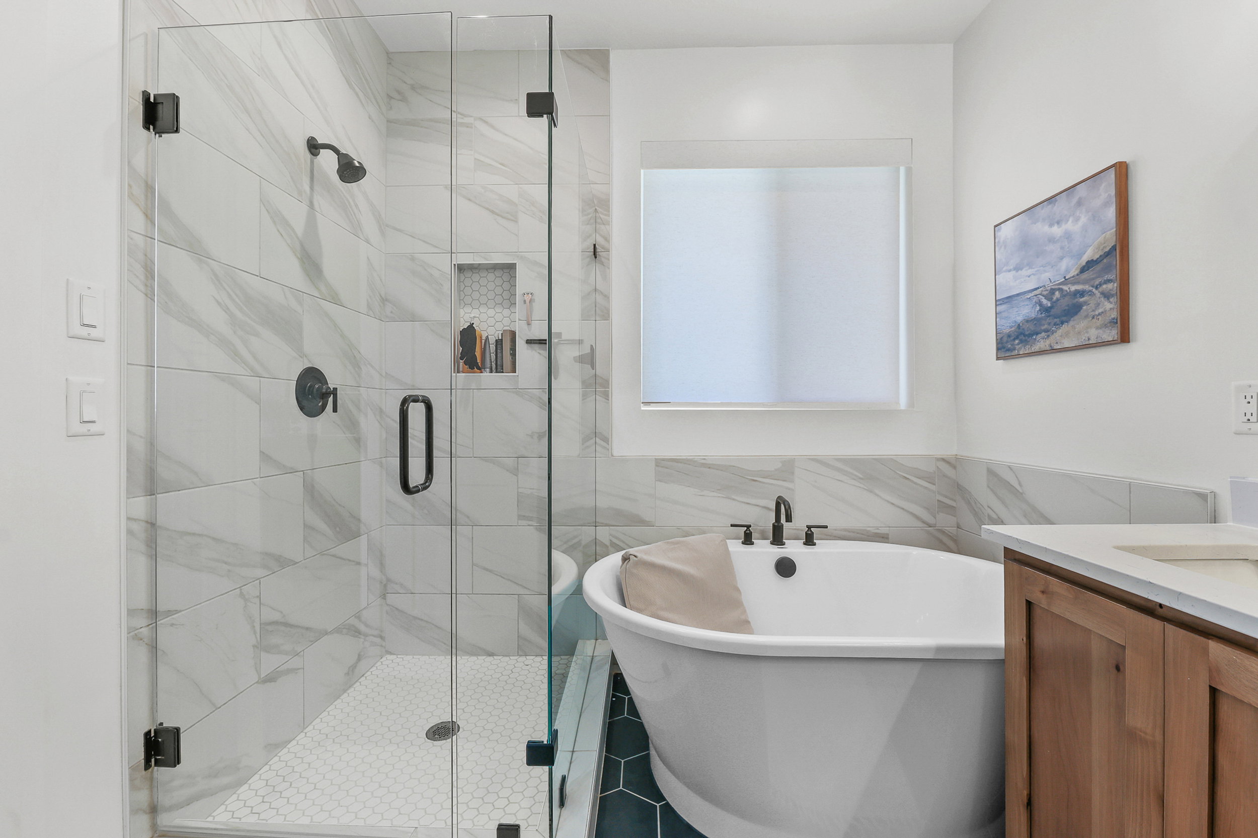 Modern bathroom featuring a frameless glass shower enclosure with matte black fixtures, a built-in shower niche, and white hexagonal floor tiles