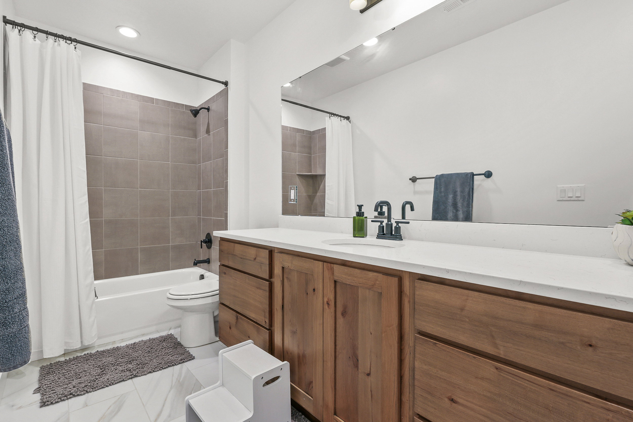 Bathroom featuring a wood-finish vanity with a white countertop, large wall-mounted mirror, and black fixtures