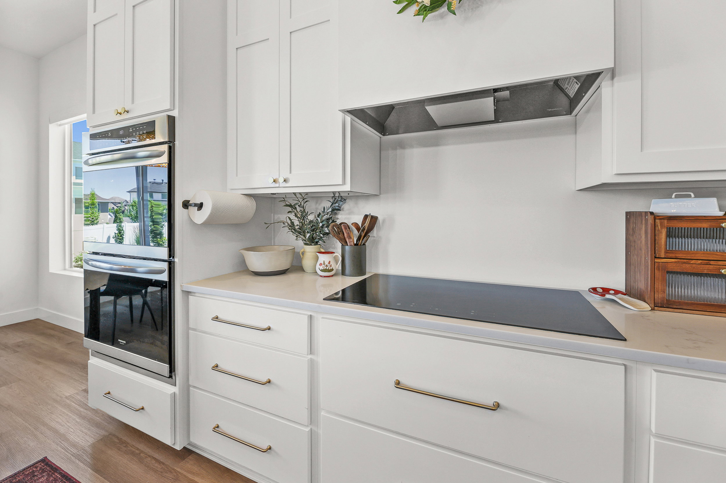 Modern kitchen featuring white shaker cabinetry, an integrated cooktop, stainless steel double wall ovens, wood-finish flooring, and light-toned countertops