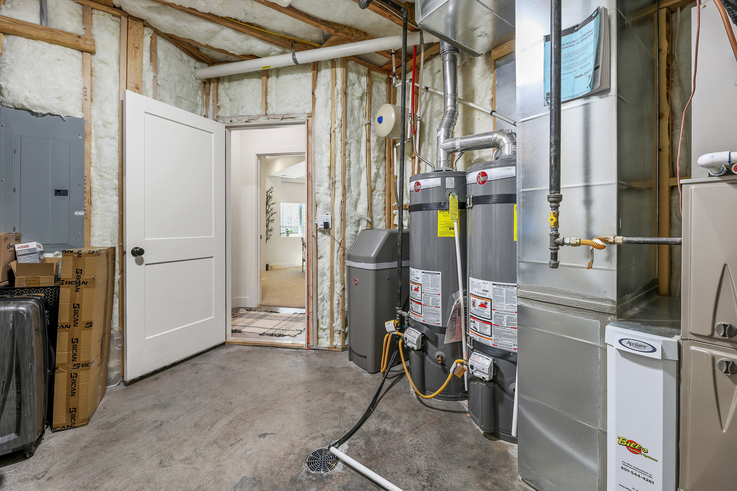 Utility room featuring two water heaters, a water softener system, HVAC furnace, and exposed insulation