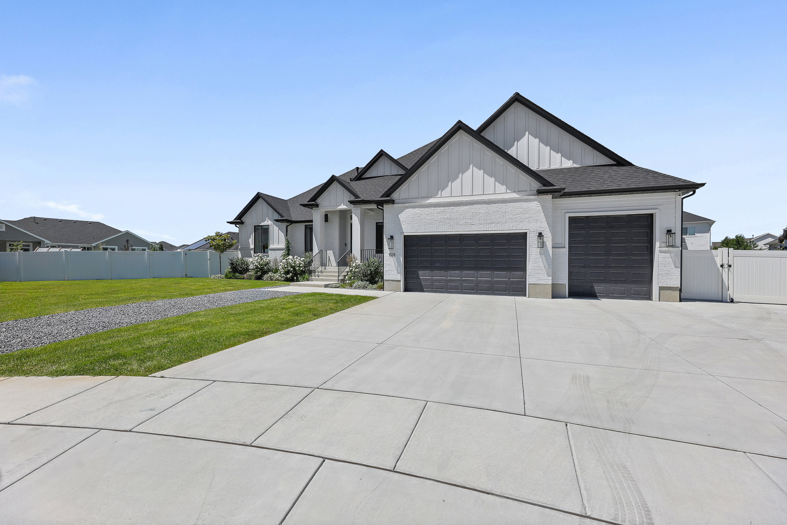 Contemporary home with a white brick and vertical siding exterior, featuring a three-car garage with dark paneled doors