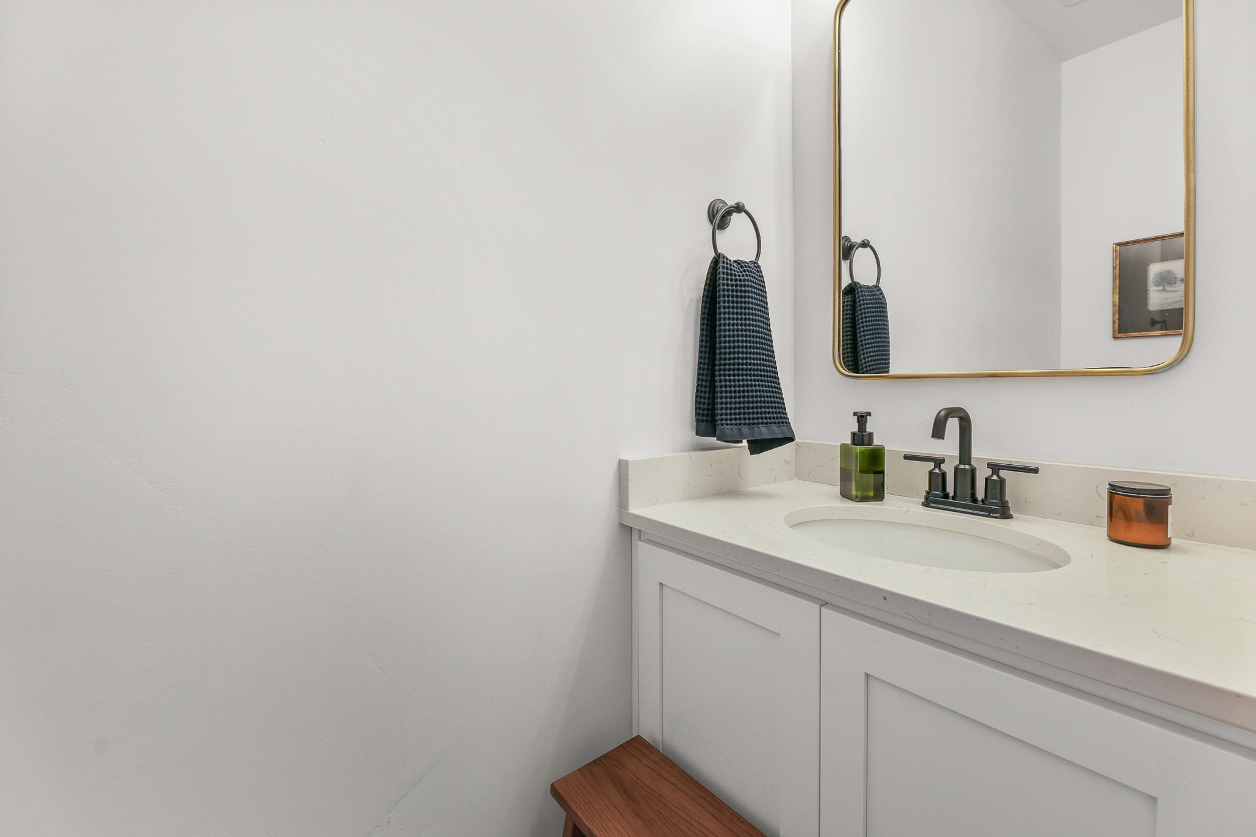 Vanity with a white countertop and integrated oval sink, featuring a matte black faucet and a gold-framed mirror
