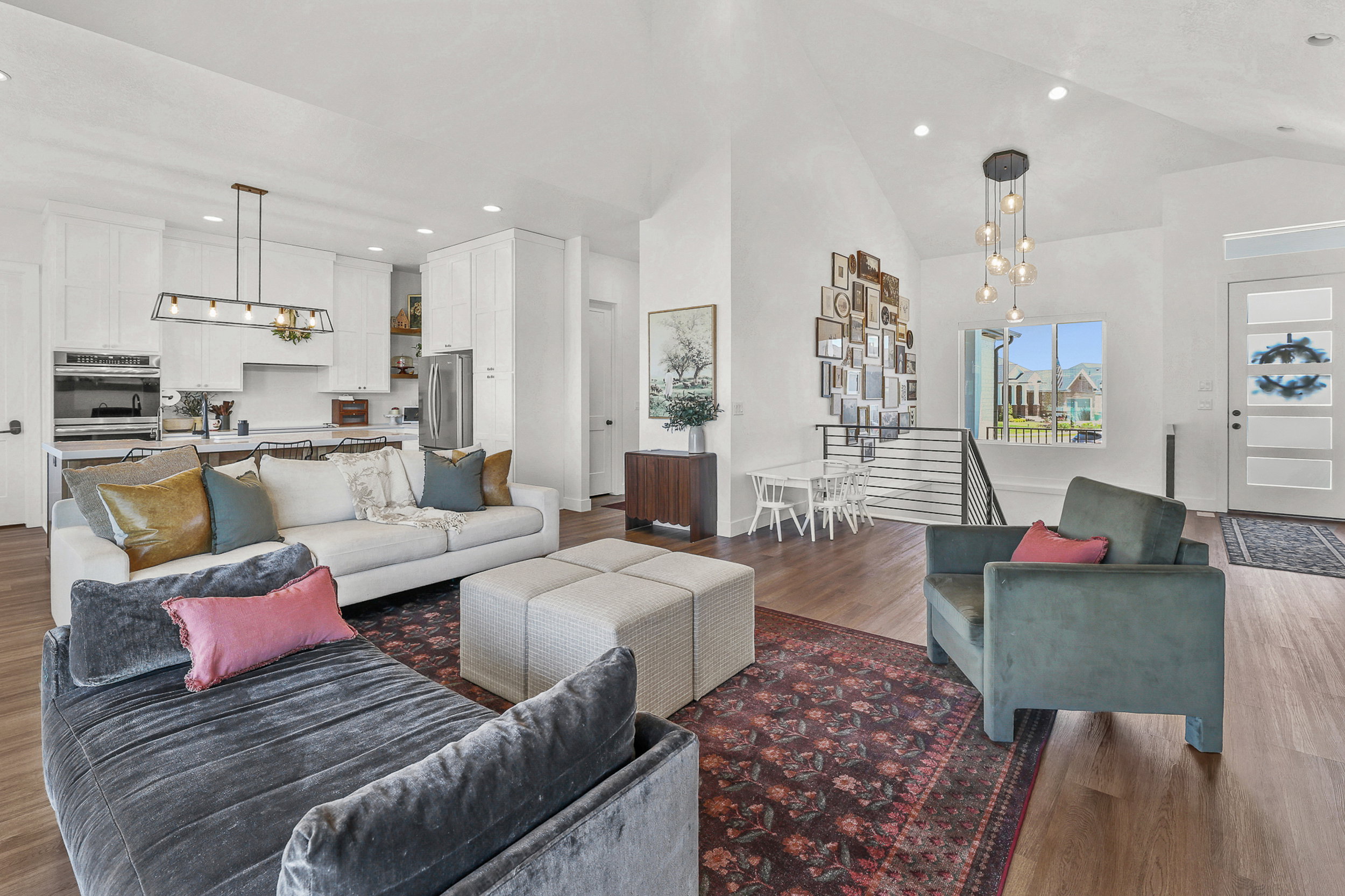 Open-concept living area featuring wood-finish flooring, vaulted ceilings with recessed lighting, and a modern tiered chandelier