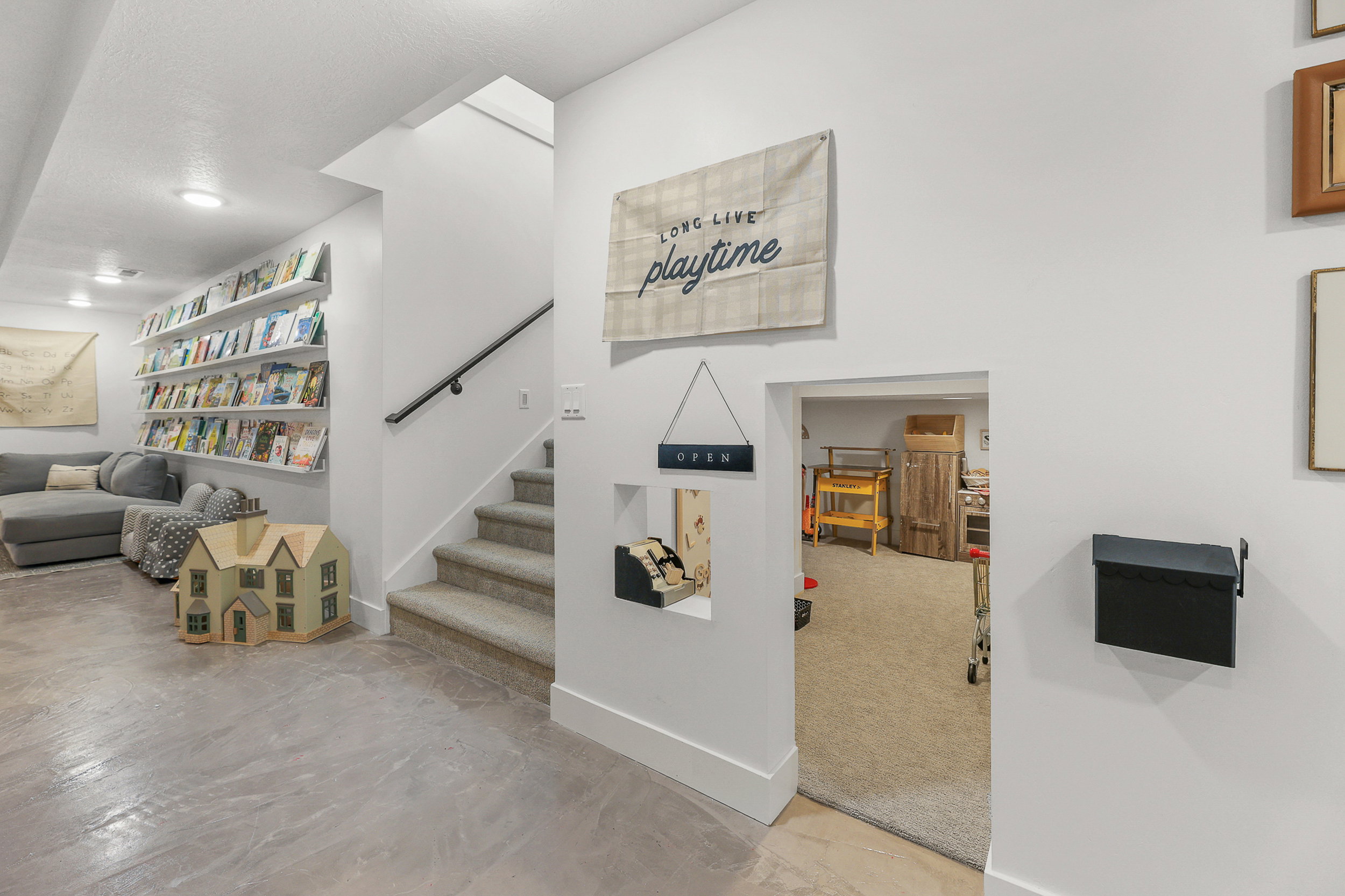 Lower-level living space featuring concrete flooring, a carpeted staircase with a black handrail, and built-in wall shelving