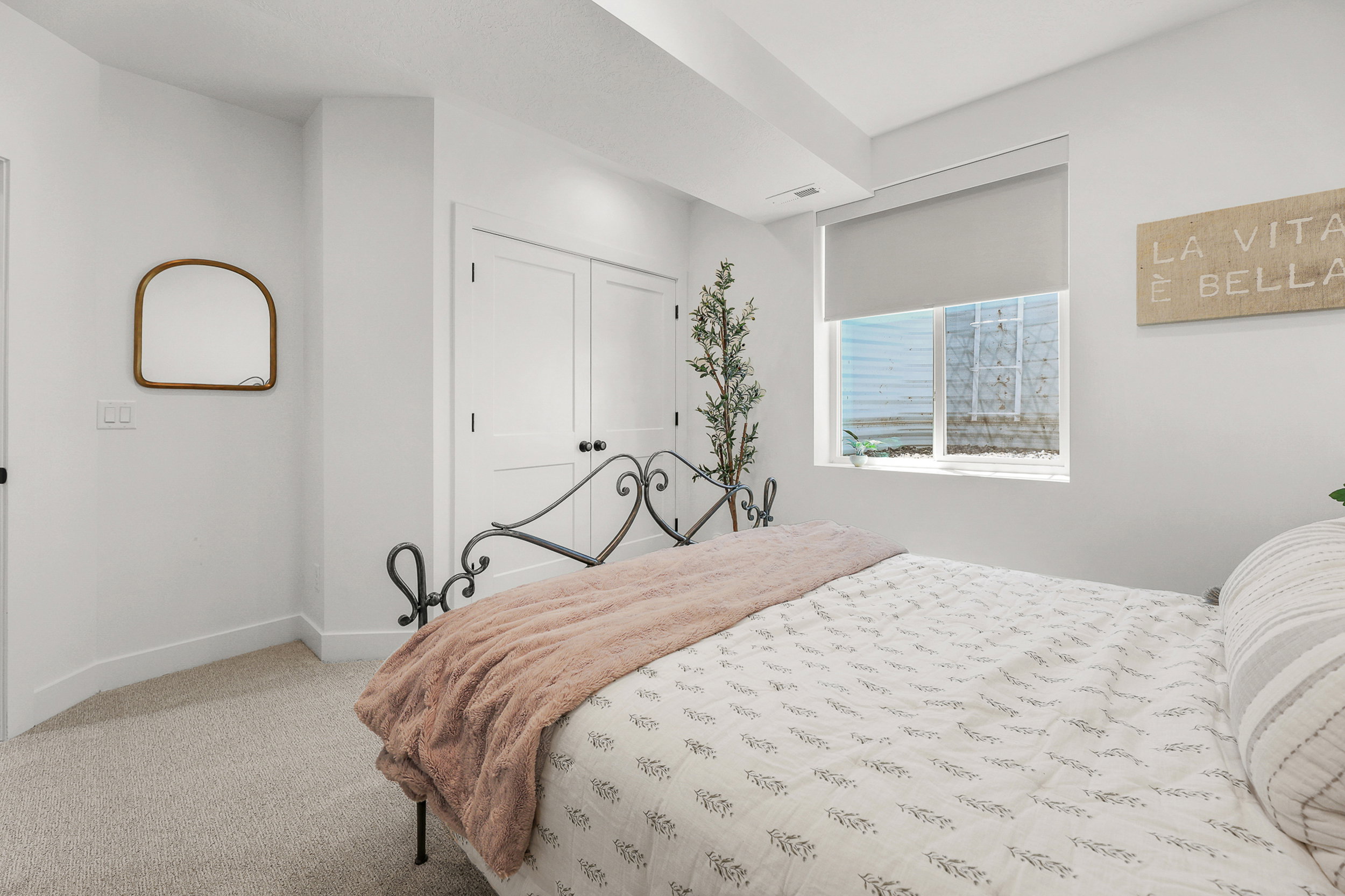 Carpeted room featuring a window with roller shade, white baseboards, and a double-door closet with black hardware