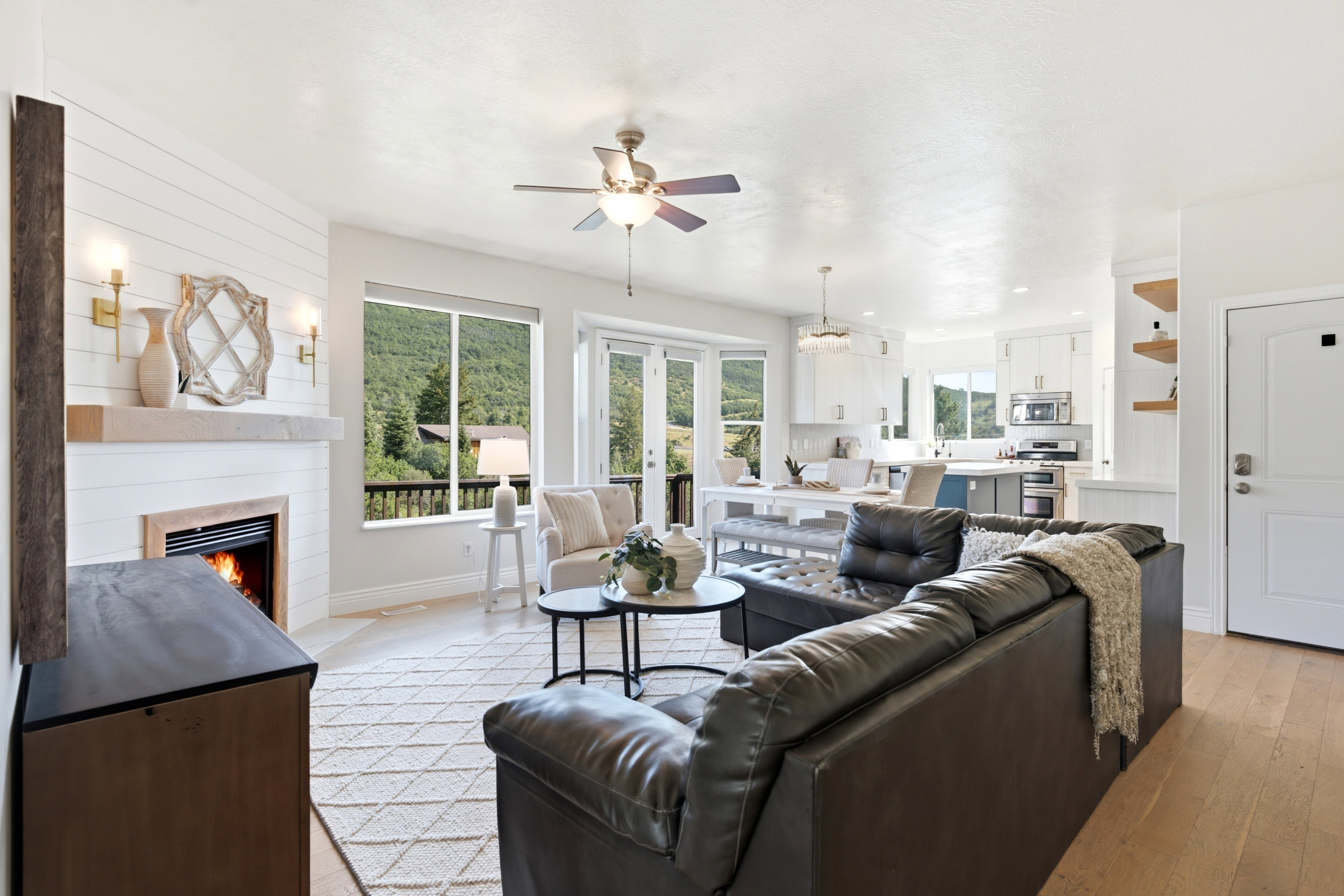 Open-concept living area featuring a shiplap fireplace with wood mantel, large windows, French doors, and wood-finish flooring