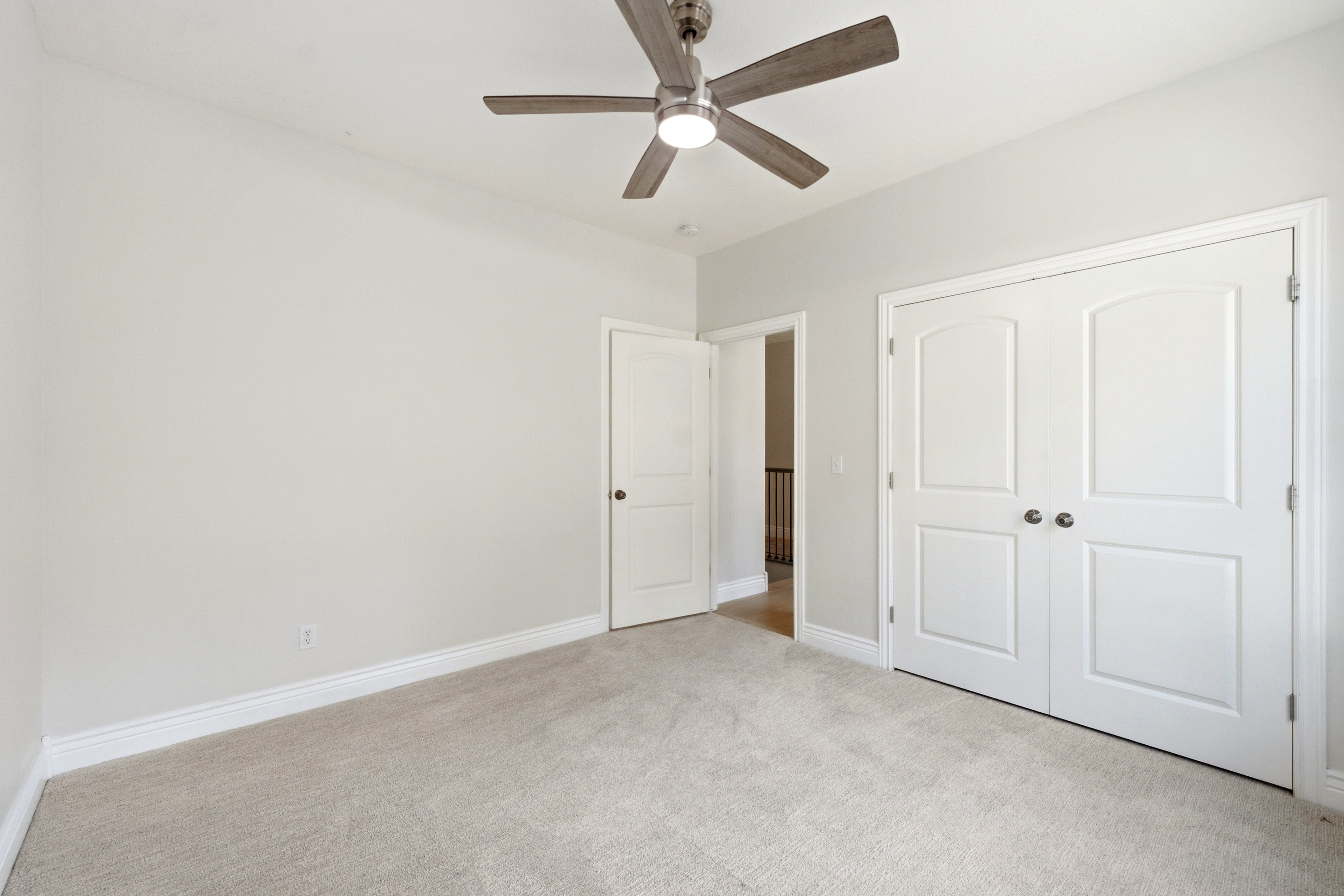 Carpeted room with a ceiling fan, white baseboards, and two white panel doors featuring dark hardware