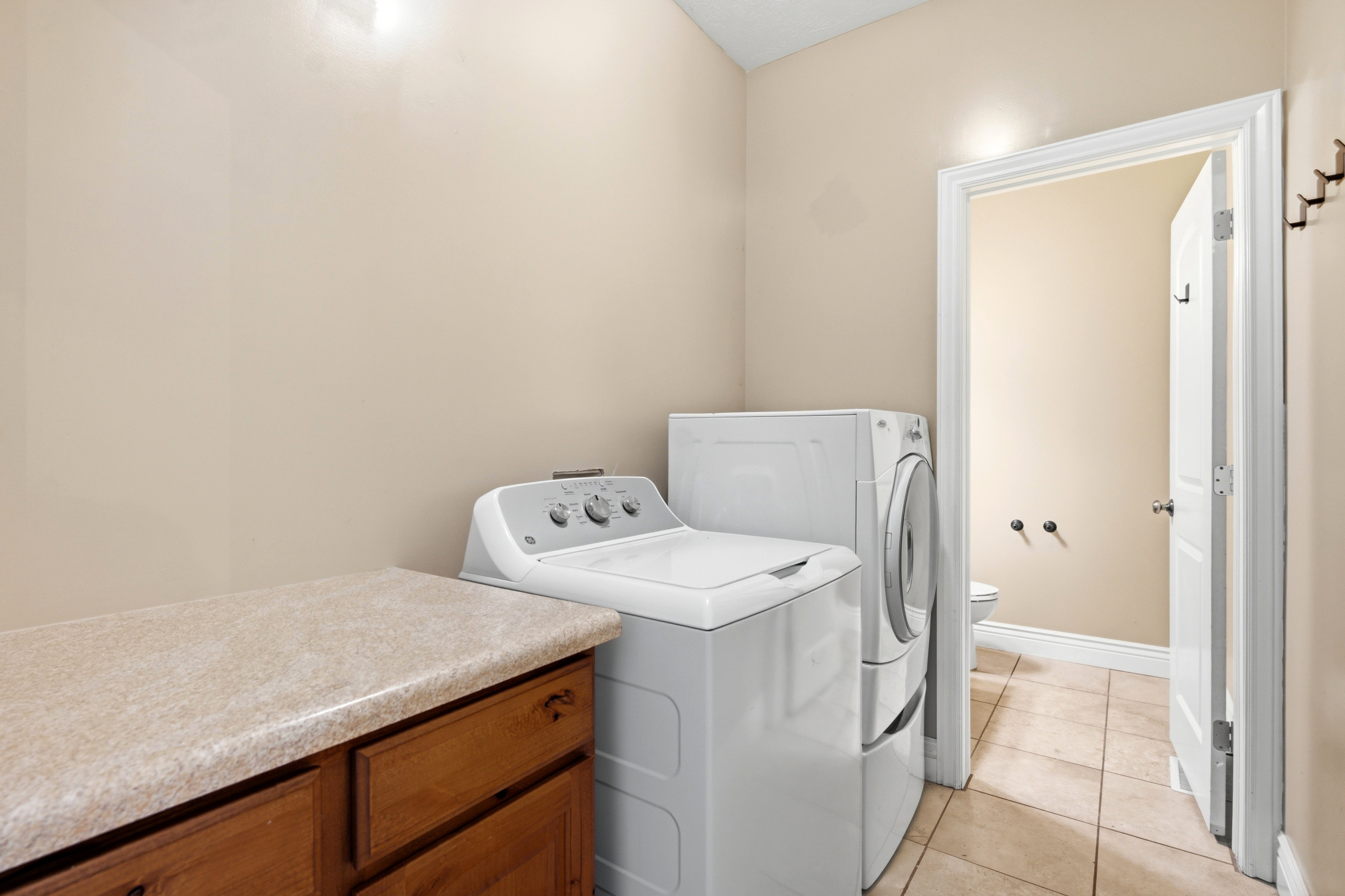 Dedicated laundry area featuring a built-in wood-finish cabinet with a light-toned countertop, and tile flooring