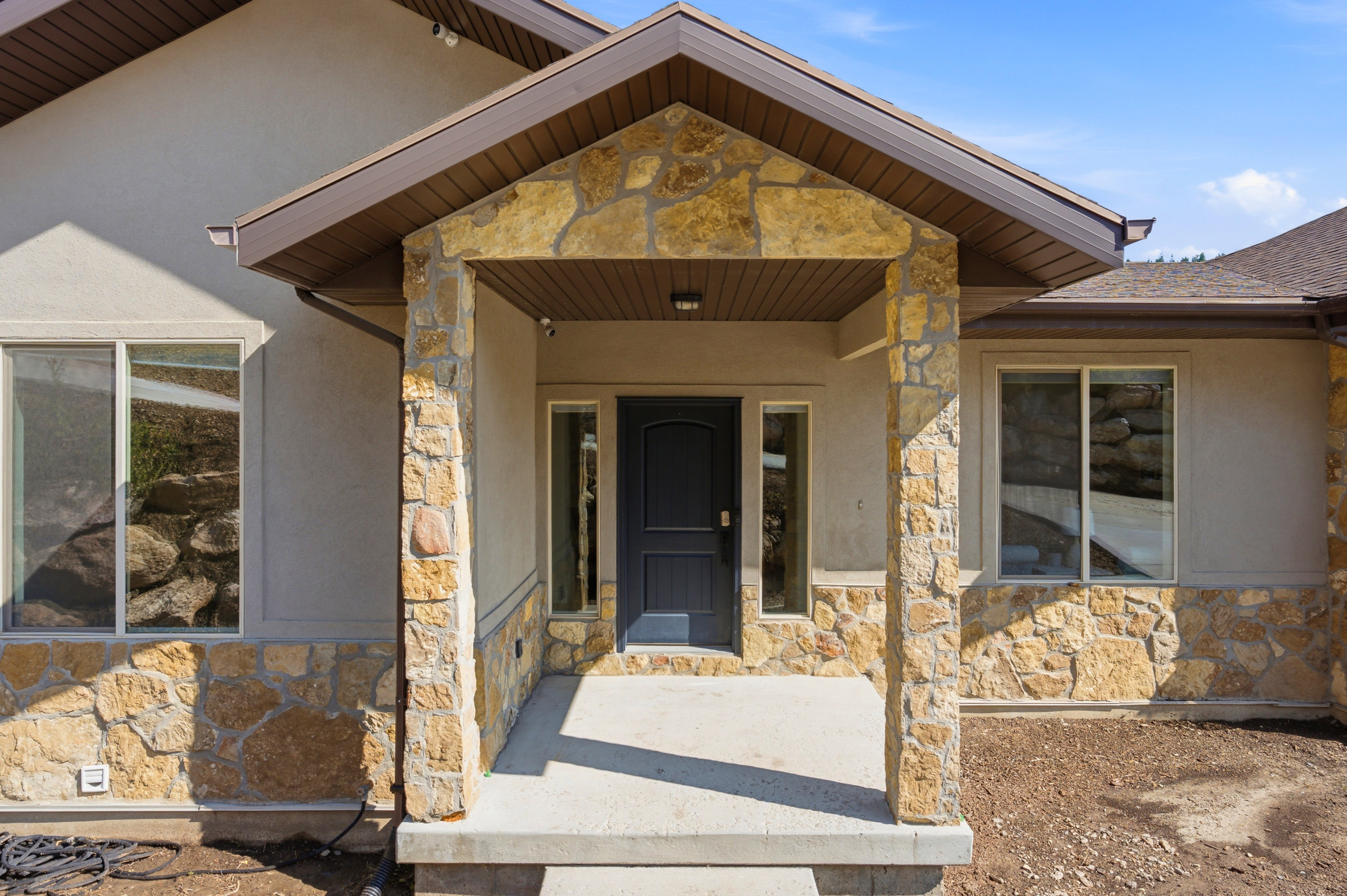 Stone and stucco exterior featuring a covered entry, dark paneled door with sidelight windows, and a concrete porch