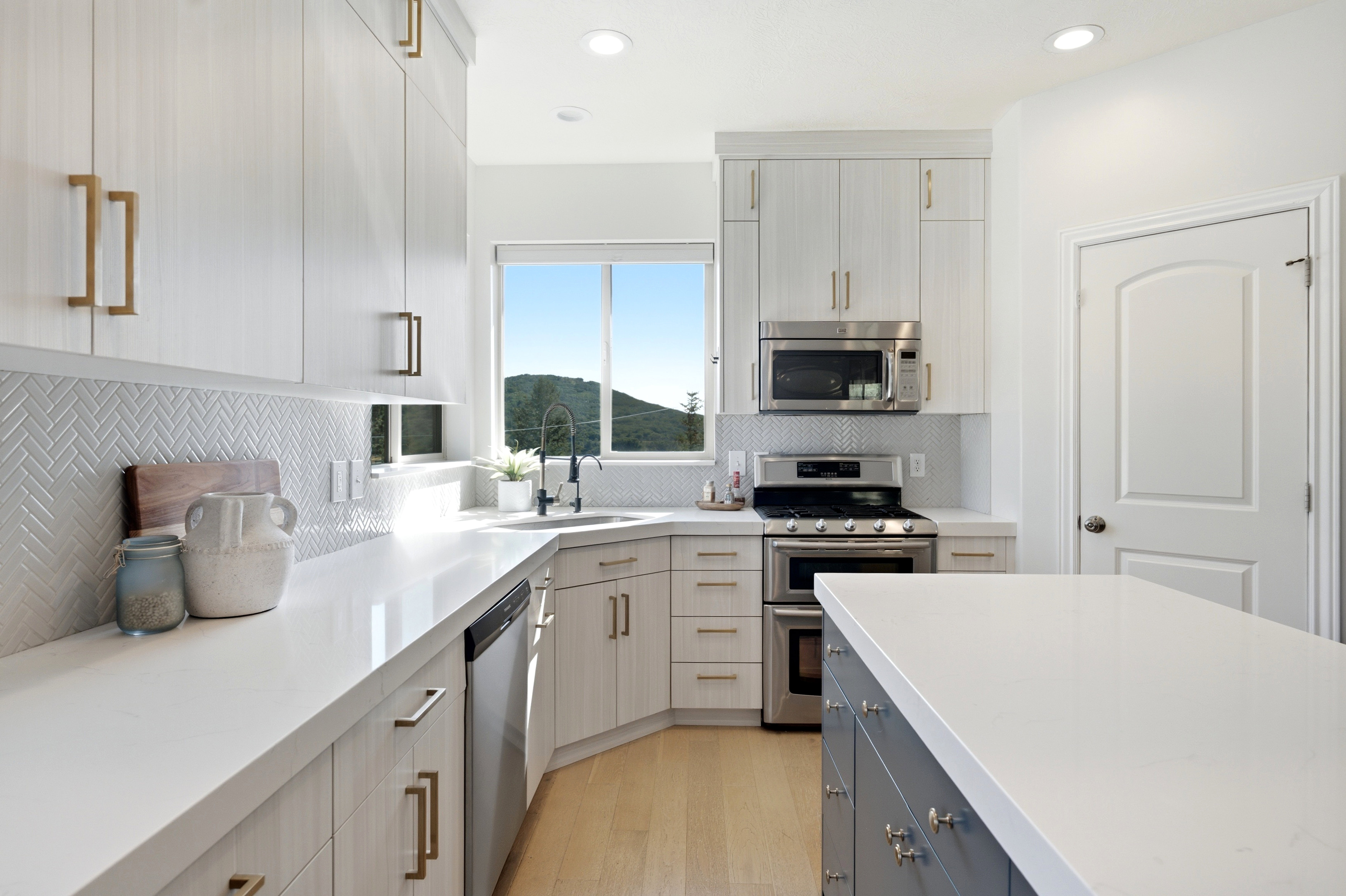 Contemporary kitchen featuring light wood-finish cabinetry with gold-tone hardware, white countertops, and a herringbone tile backsplash