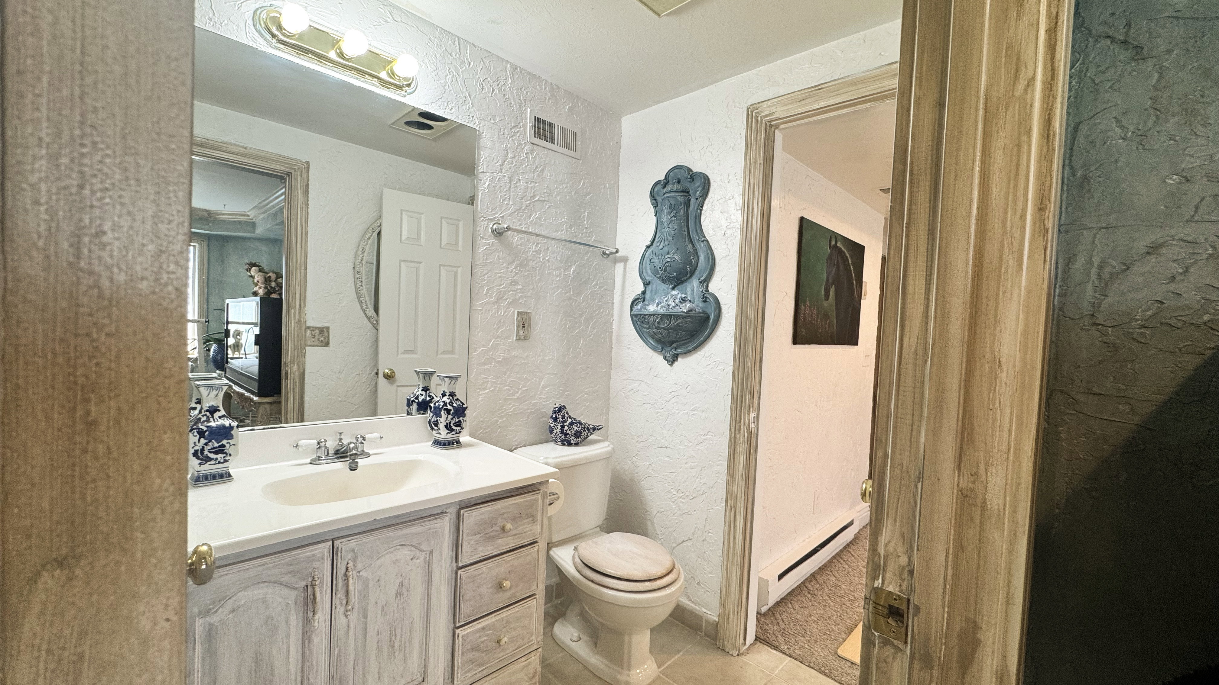 Bathroom featuring a single vanity with an integrated sink, a large wall-mounted mirror, a two-piece toilet, and textured wall finishes