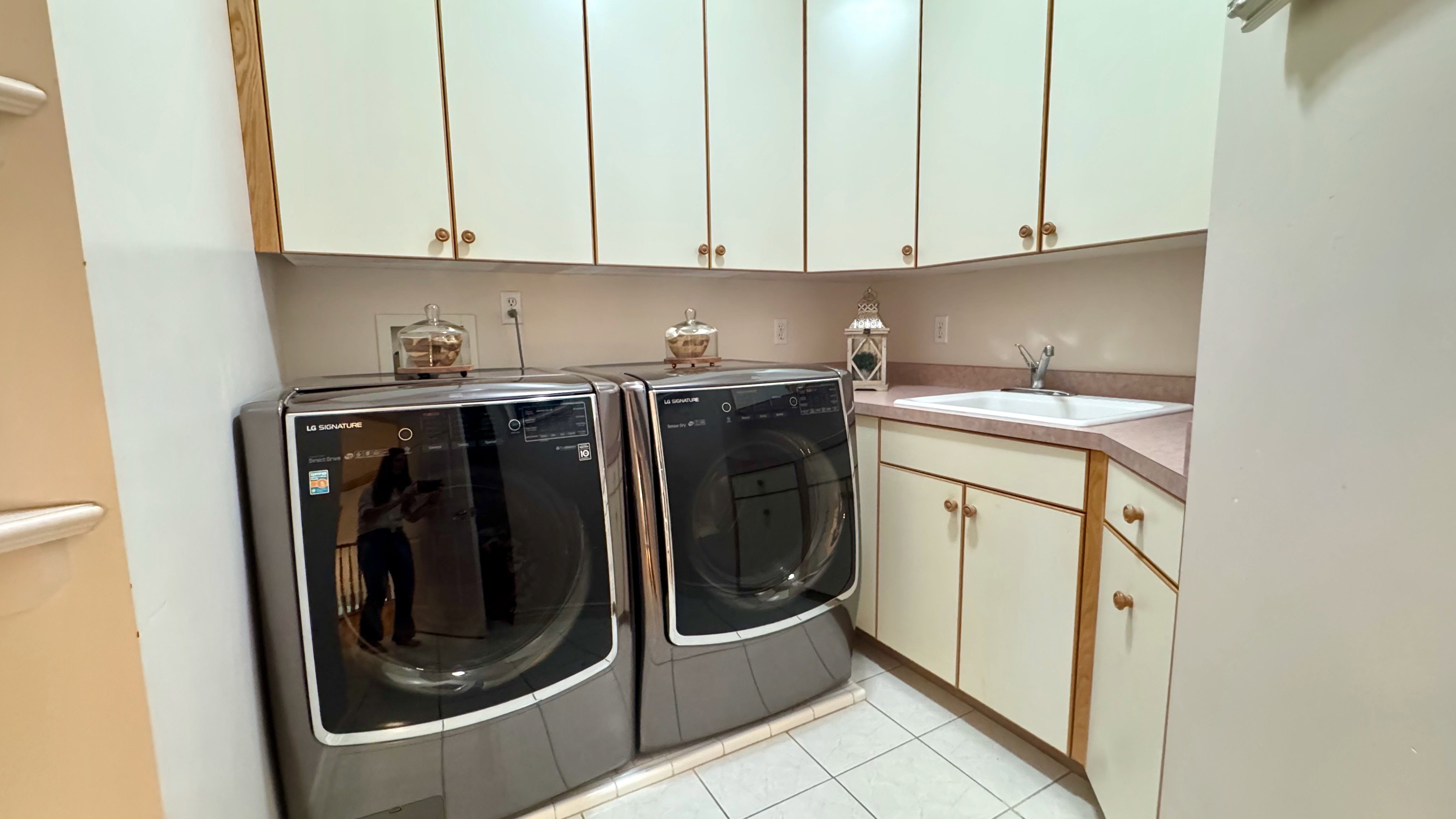 Dedicated laundry area featuring a utility sink, white tiled flooring, and ample cabinetry with wood-finish trim