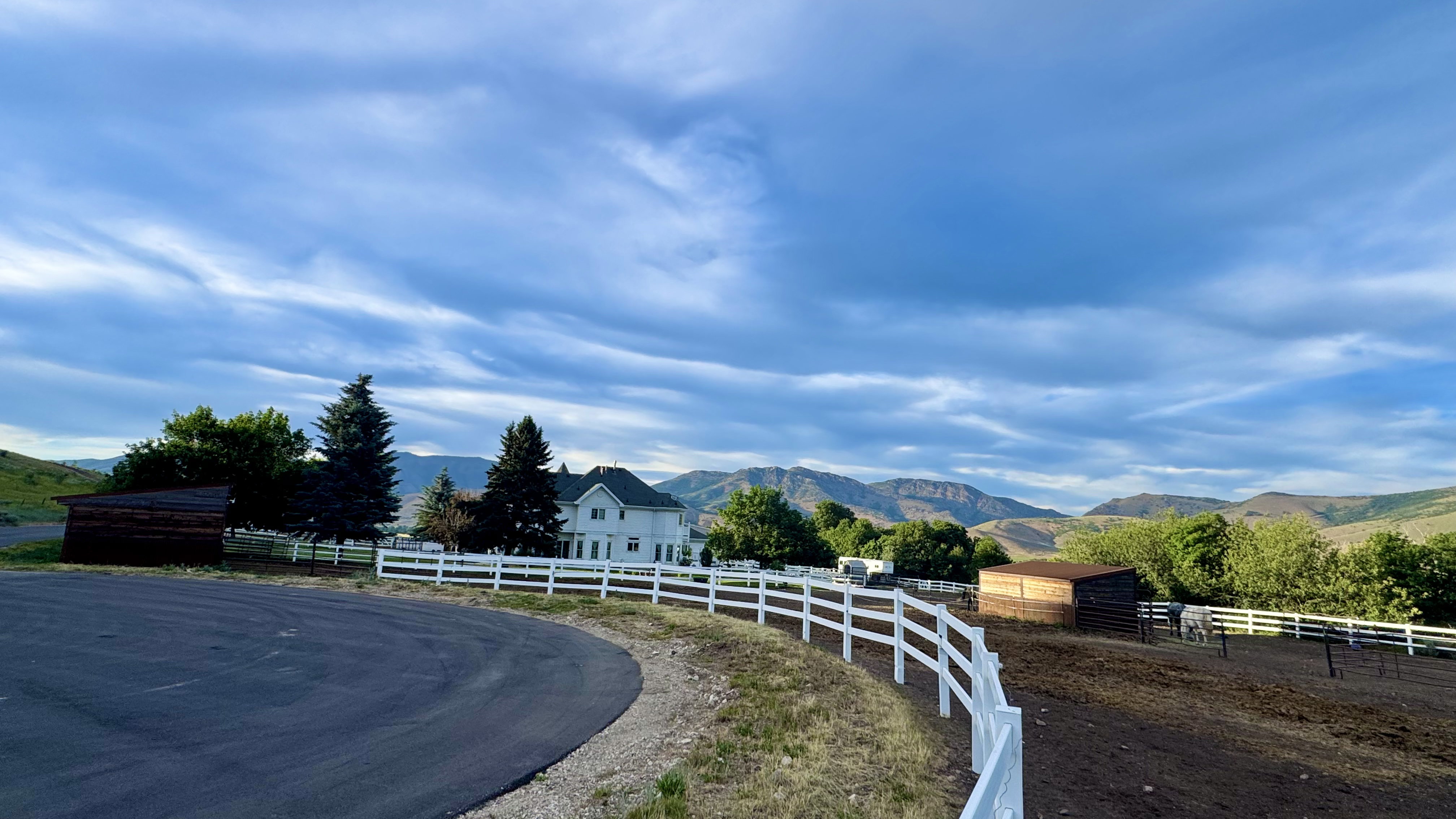 Expansive property featuring a white picket fence, a large barn structure, an asphalt drive, and mature trees