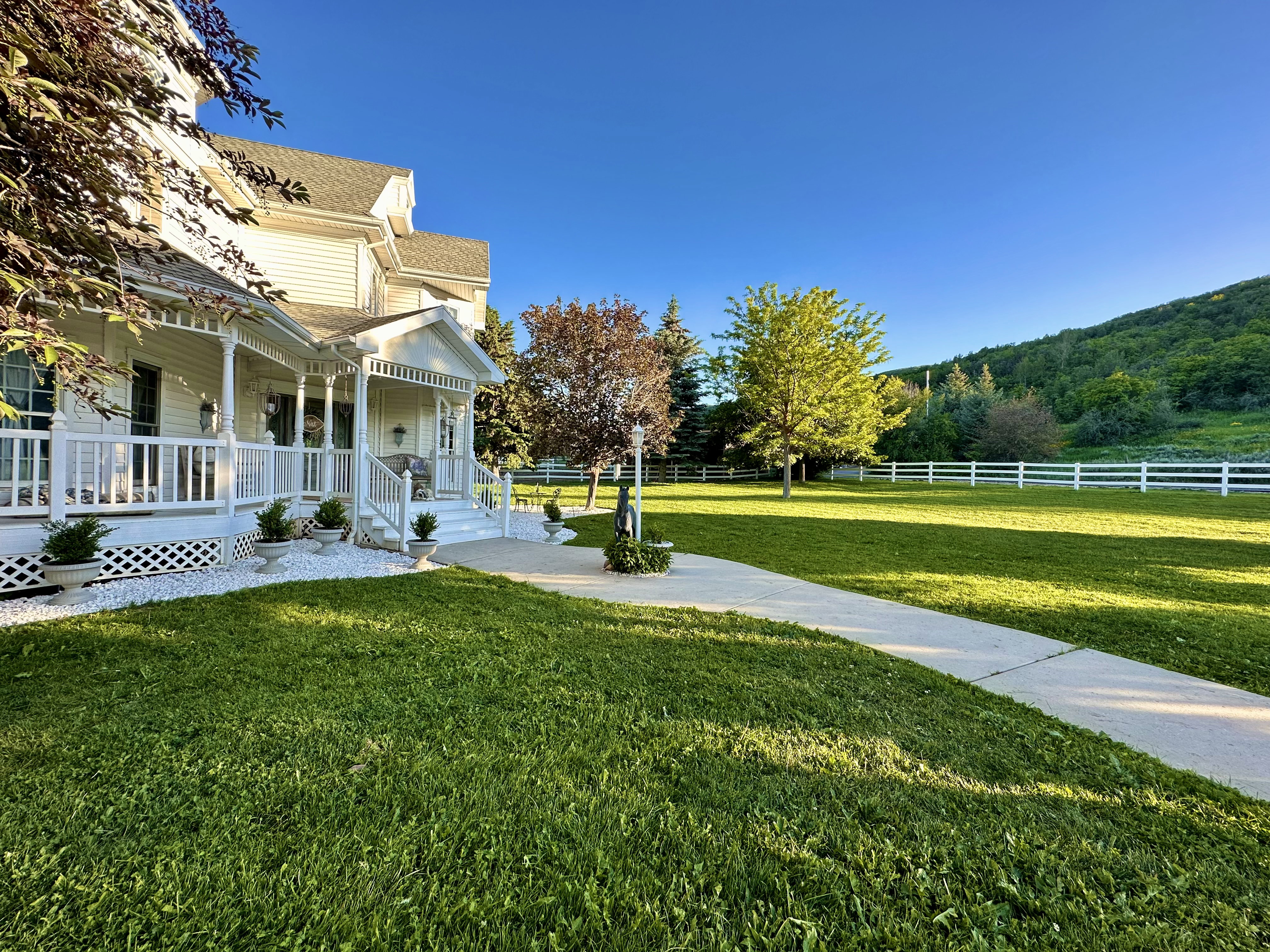 White vinyl siding residence featuring a wraparound porch with white railings, a concrete pathway, and a sprawling green lawn