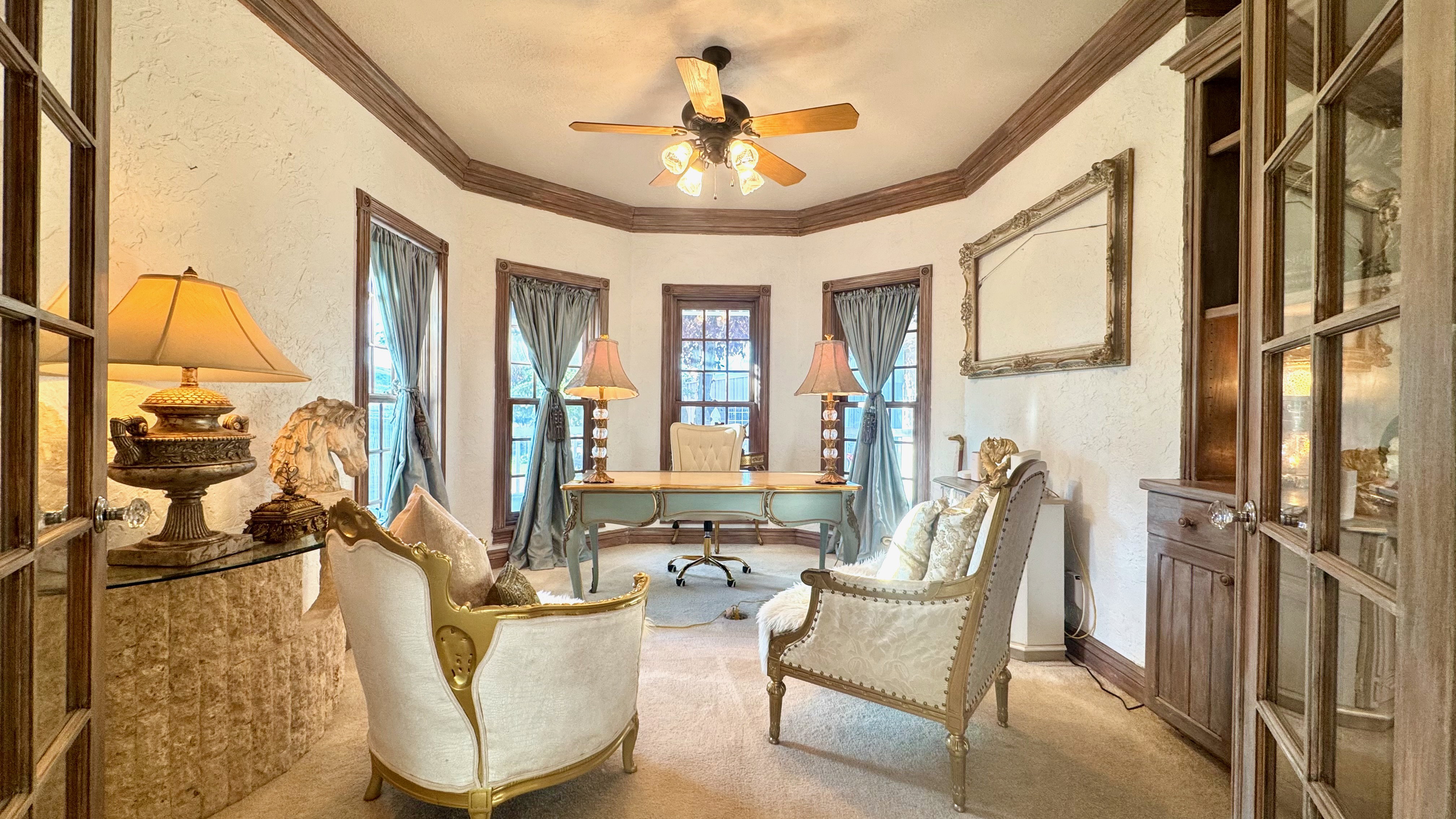 Formal room featuring textured walls, multiple windows, a ceiling fan, and built-in wood cabinetry with glass doors