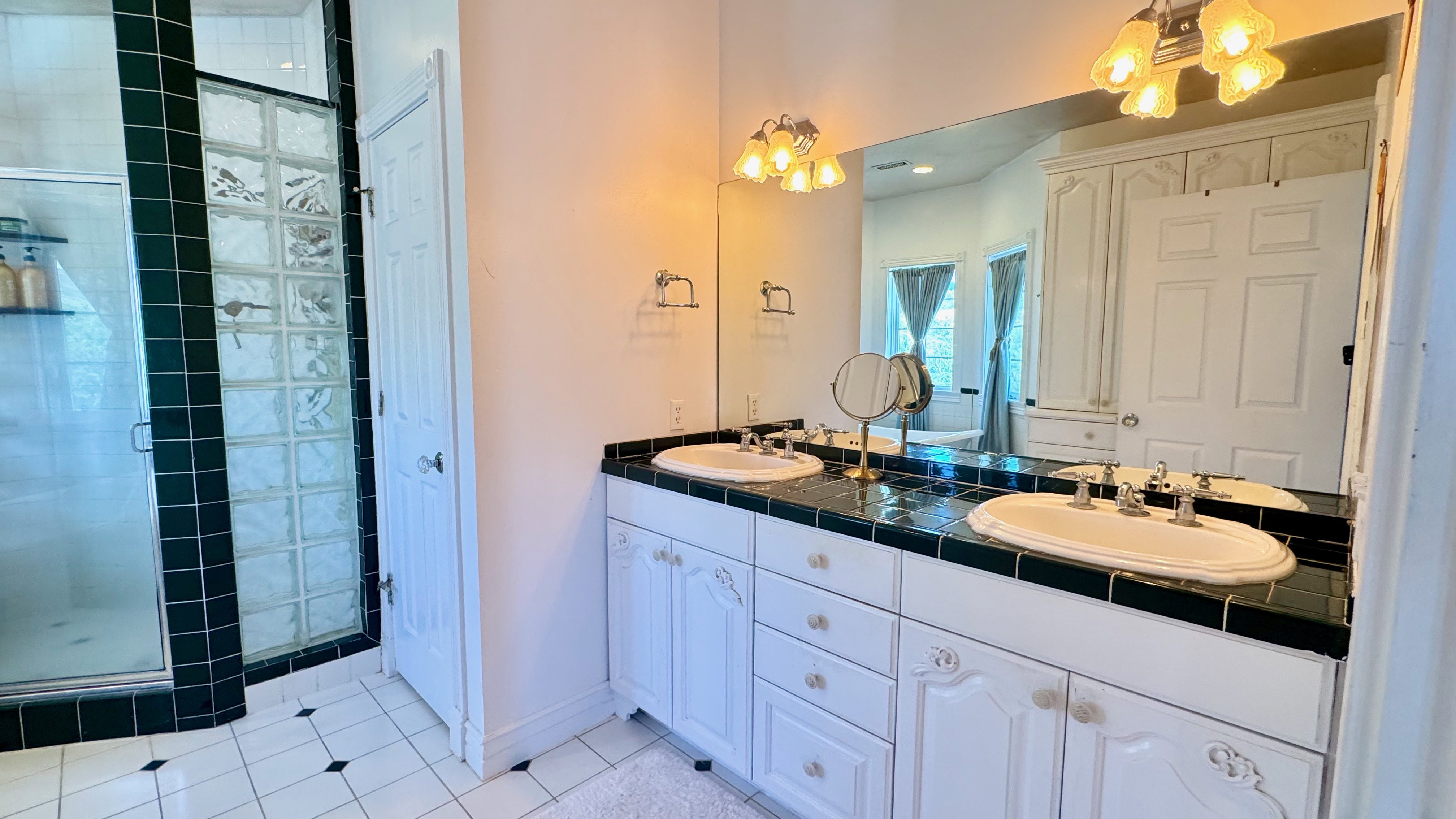 Dual vanity with drop-in sinks, black tiled countertop, and white cabinetry
