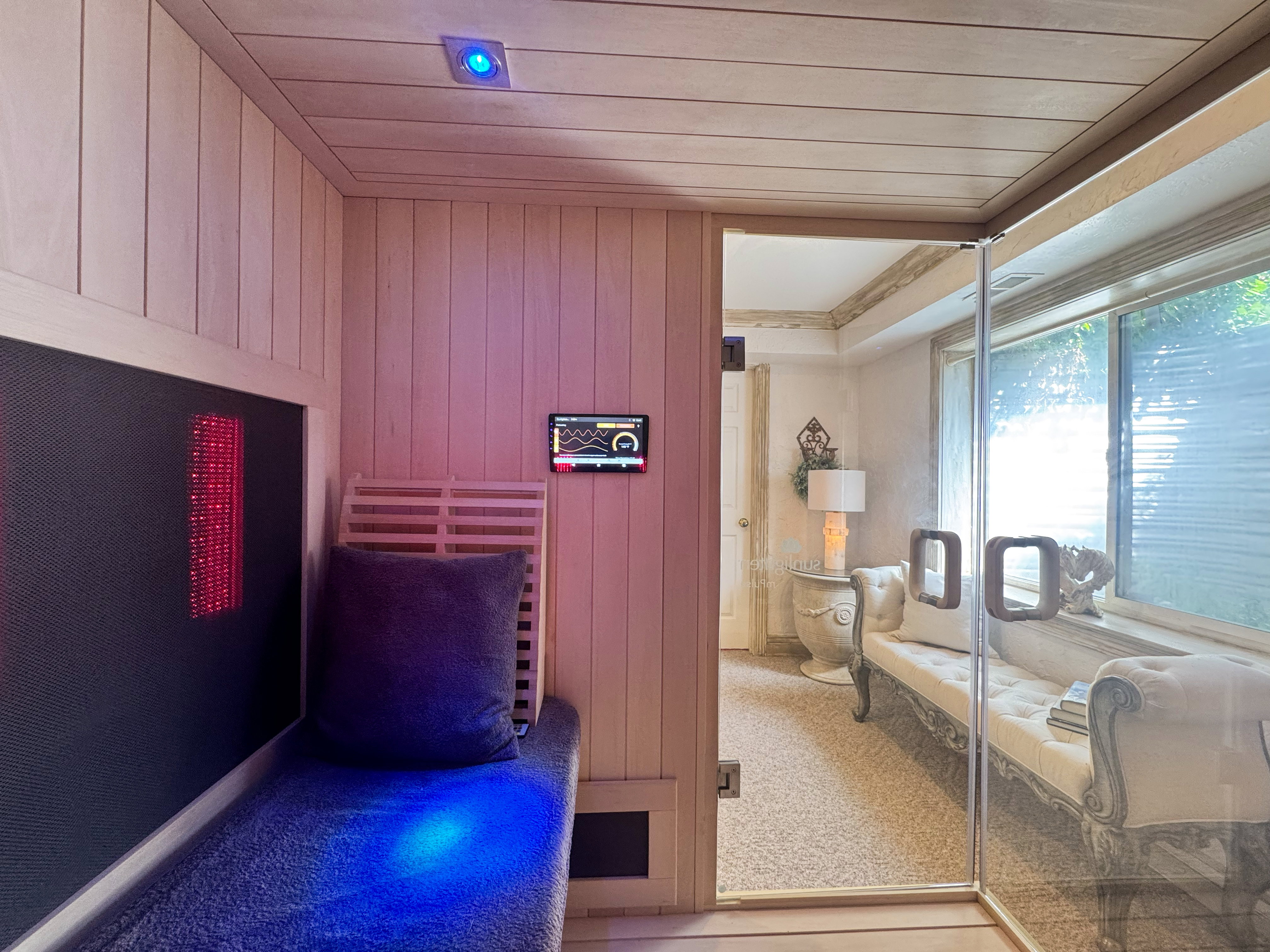 Custom sauna featuring wood paneling, built-in bench seating, integrated lighting, and a glass entry door