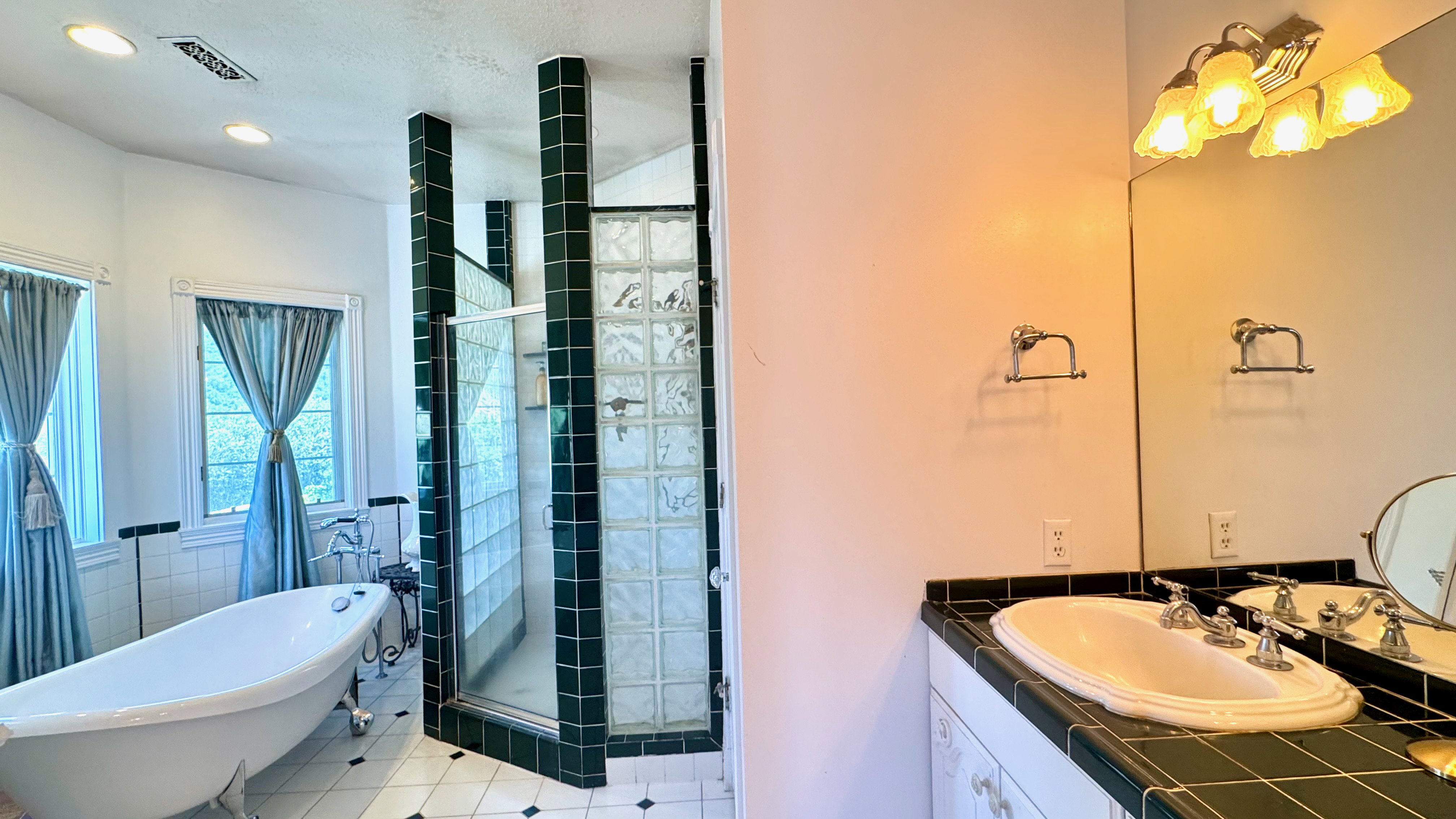 Bathroom featuring a freestanding clawfoot tub, a walk-in shower with glass block walls and dark green tile accents, and a vanity with a drop-in sink and dark green tile countertop