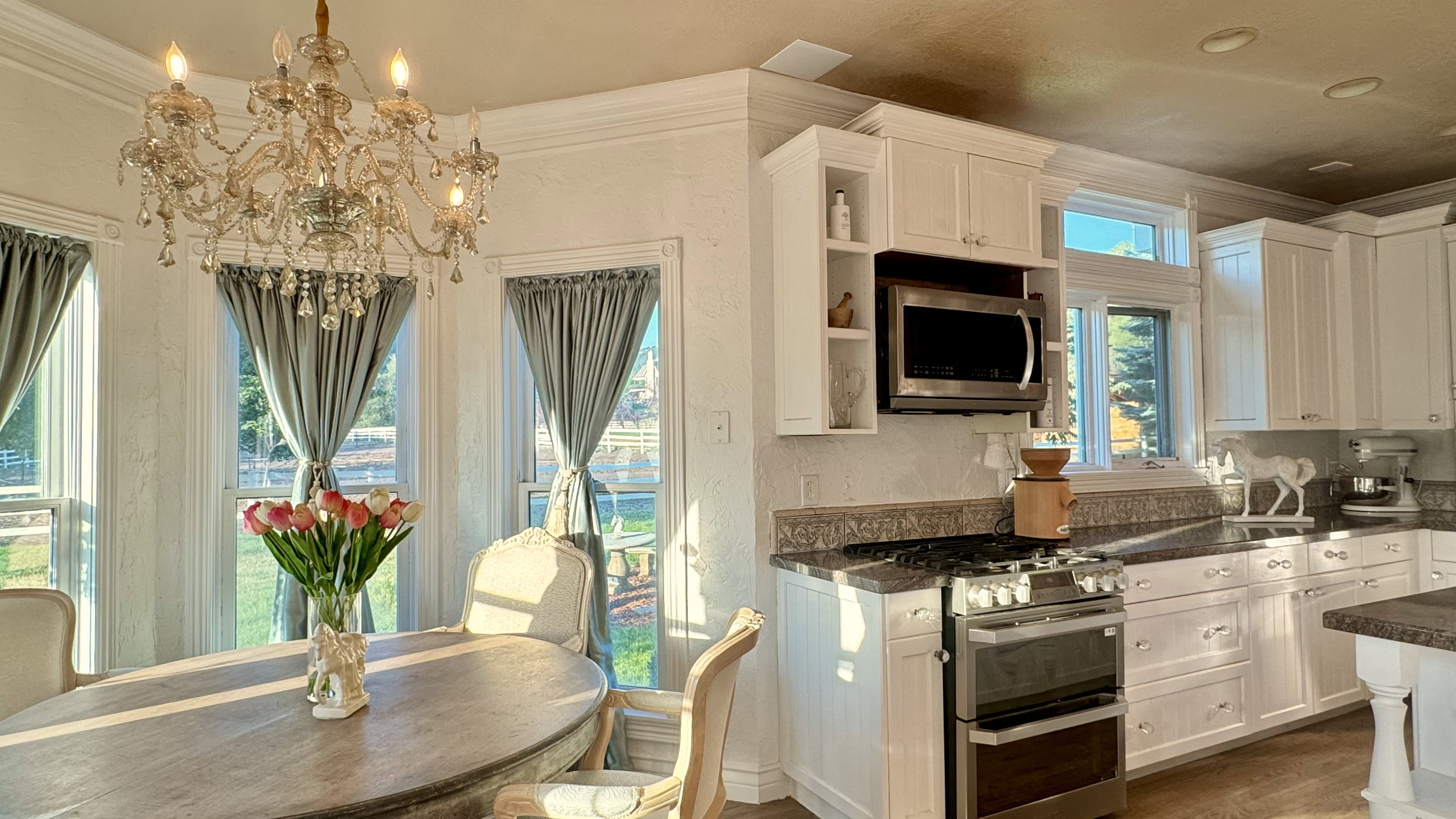 Kitchen and dining area featuring a crystal chandelier, white cabinetry, stainless steel range and microwave, and dark countertop surfaces