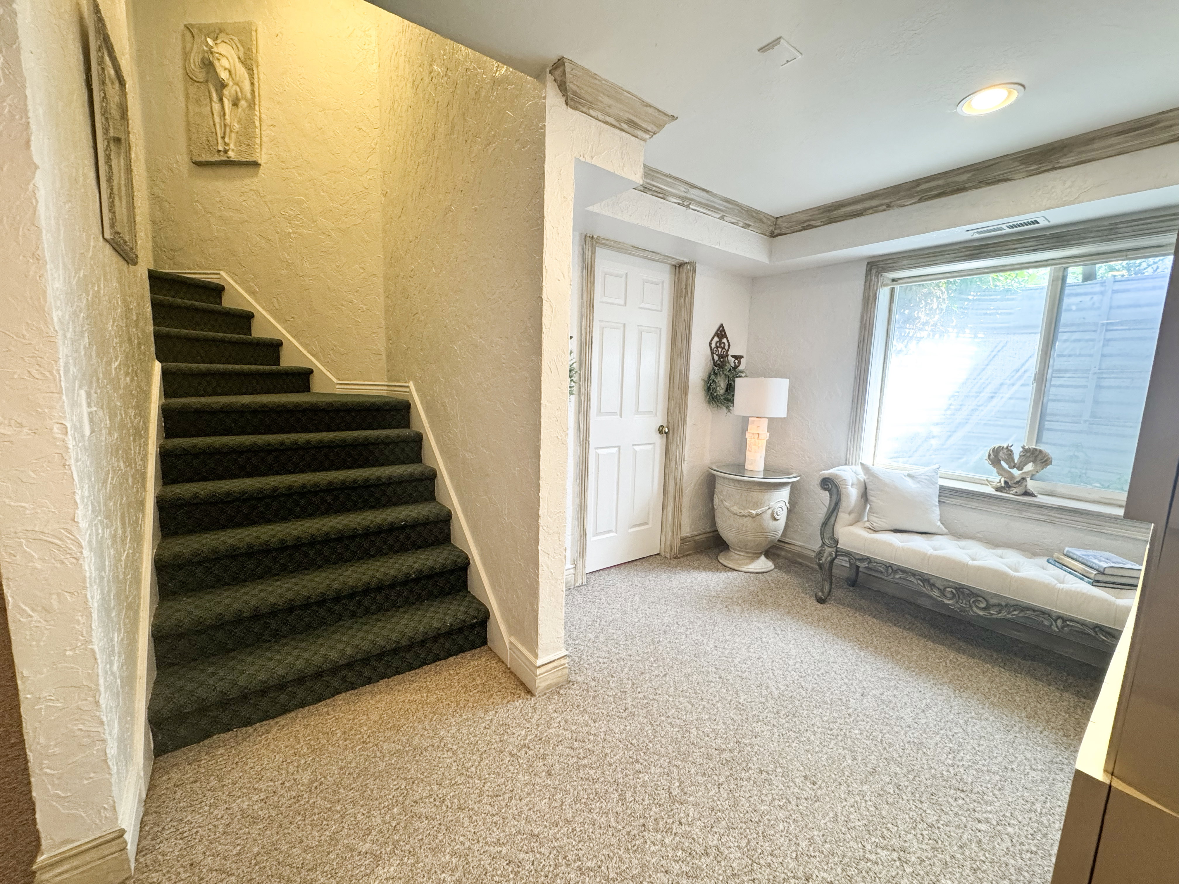 Carpeted stairway with a white handrail, textured walls, and a window with a deep sill