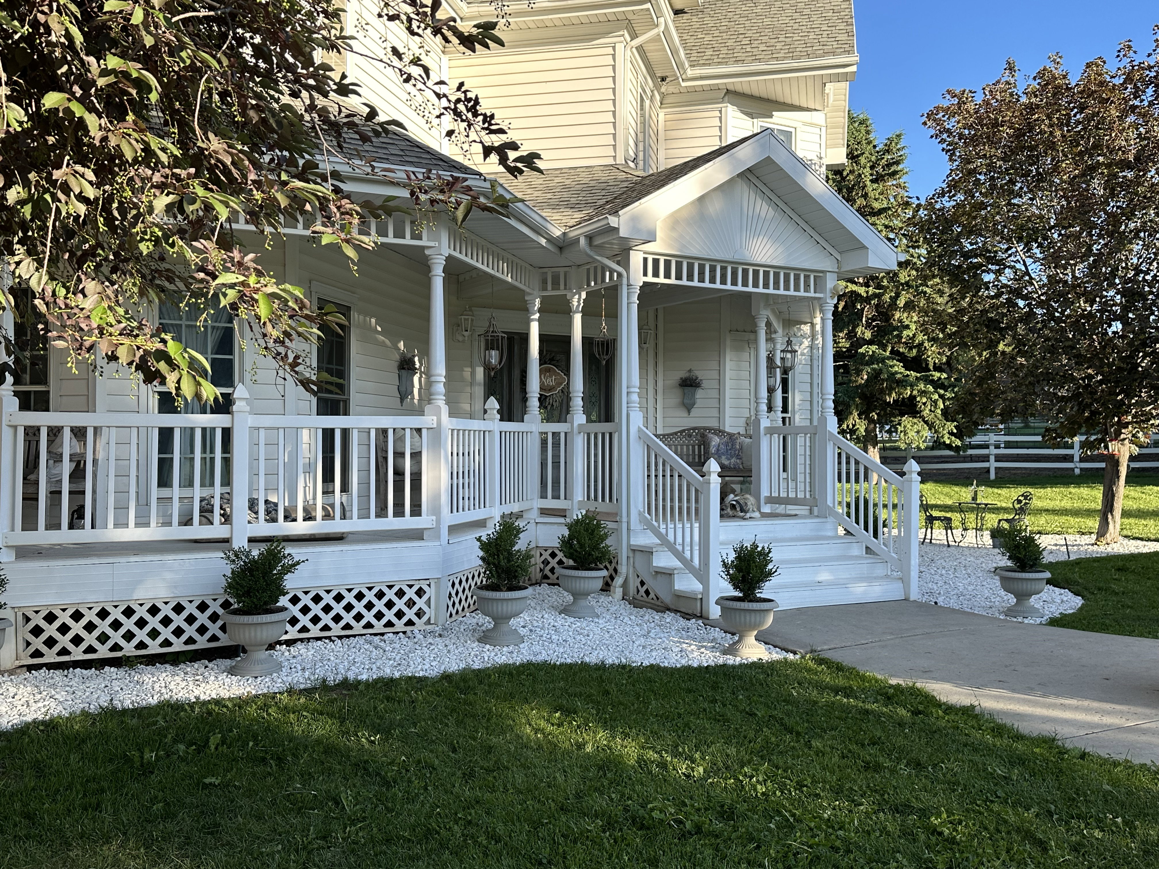 Inviting Victorian-style front porch with white railings and lattice skirting, featuring a gabled entryway and exterior wall sconces