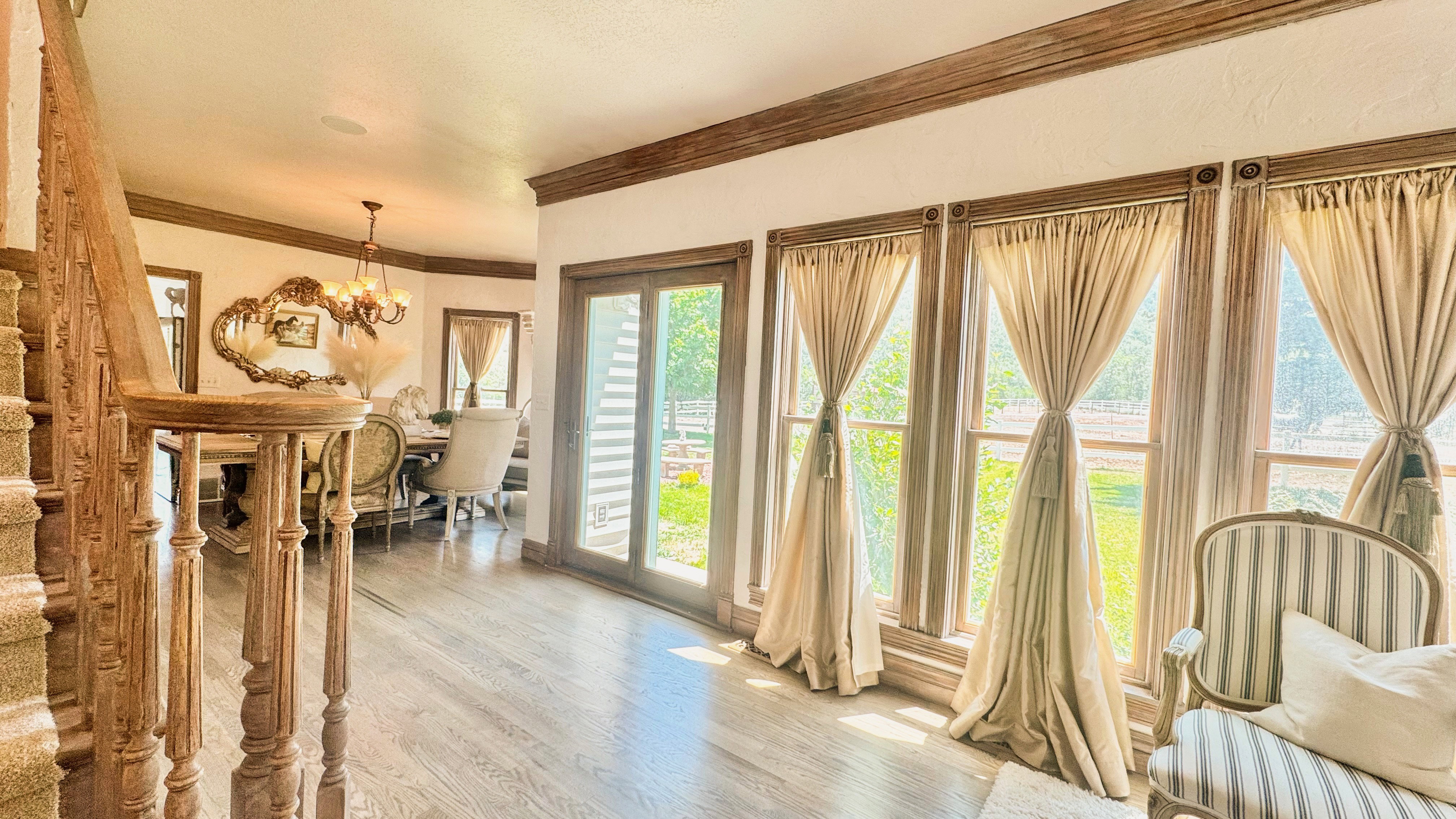 Spacious foyer featuring wood-finish flooring, an ornate carved wood staircase, and extensive window treatments