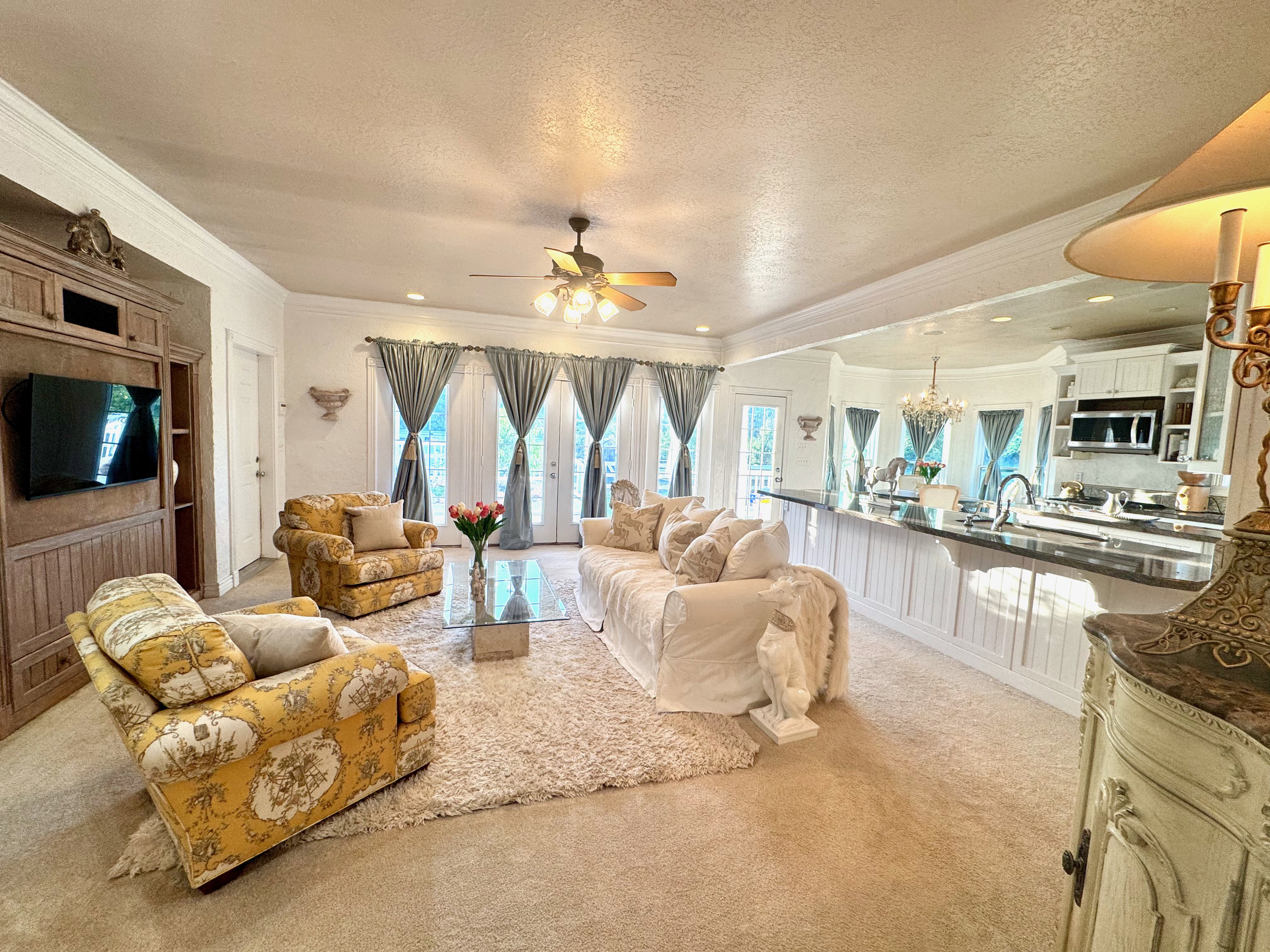Open-concept living space with light-toned carpeting, a built-in entertainment center, a ceiling fan, and multiple French doors