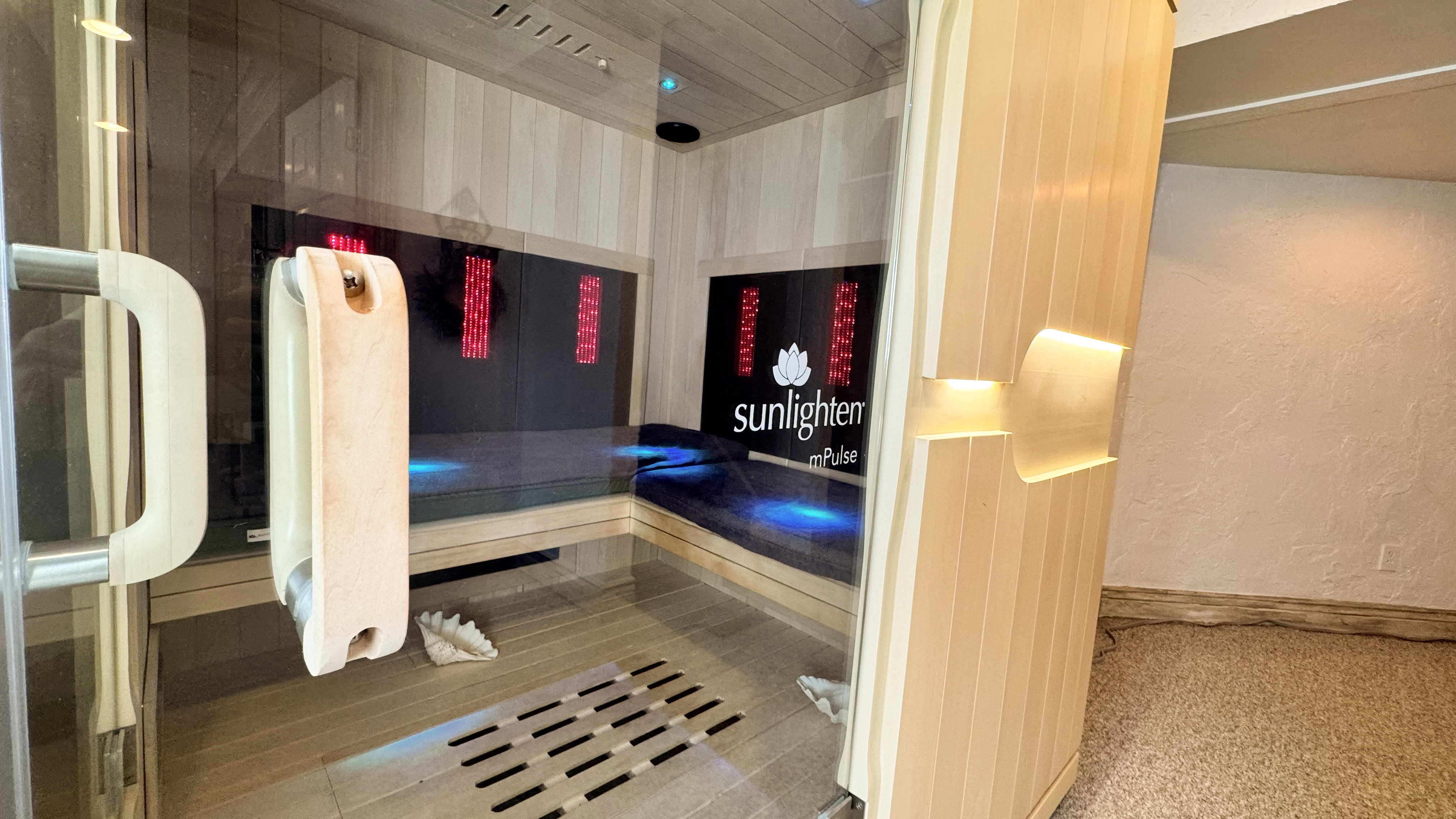 Integrated sauna featuring a glass door, light wood paneling, built-in bench seating, and interior lighting