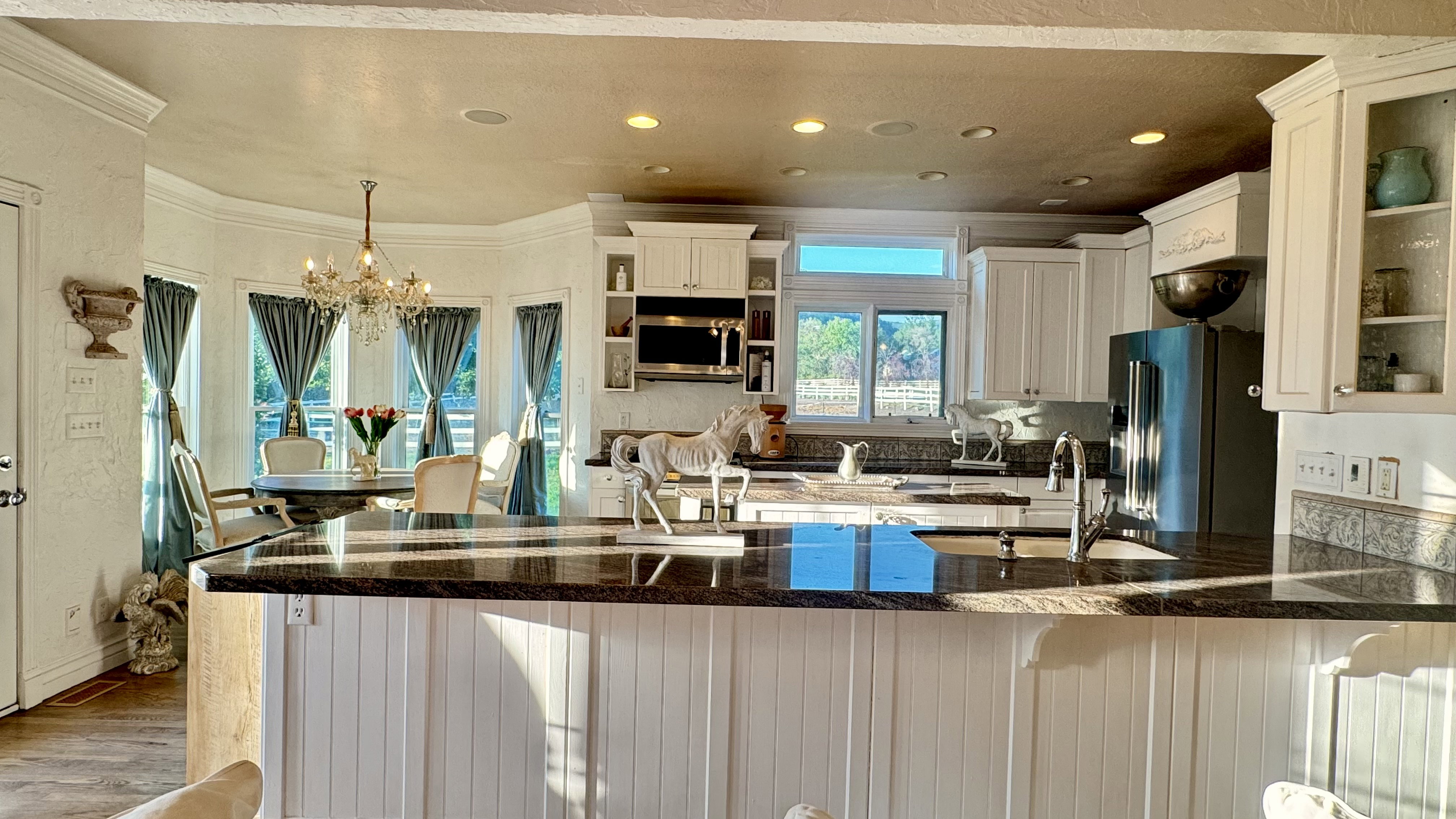 Open-concept kitchen featuring white cabinetry, dark stone countertops, stainless steel appliances, a kitchen island with beadboard paneling, and recessed lighting