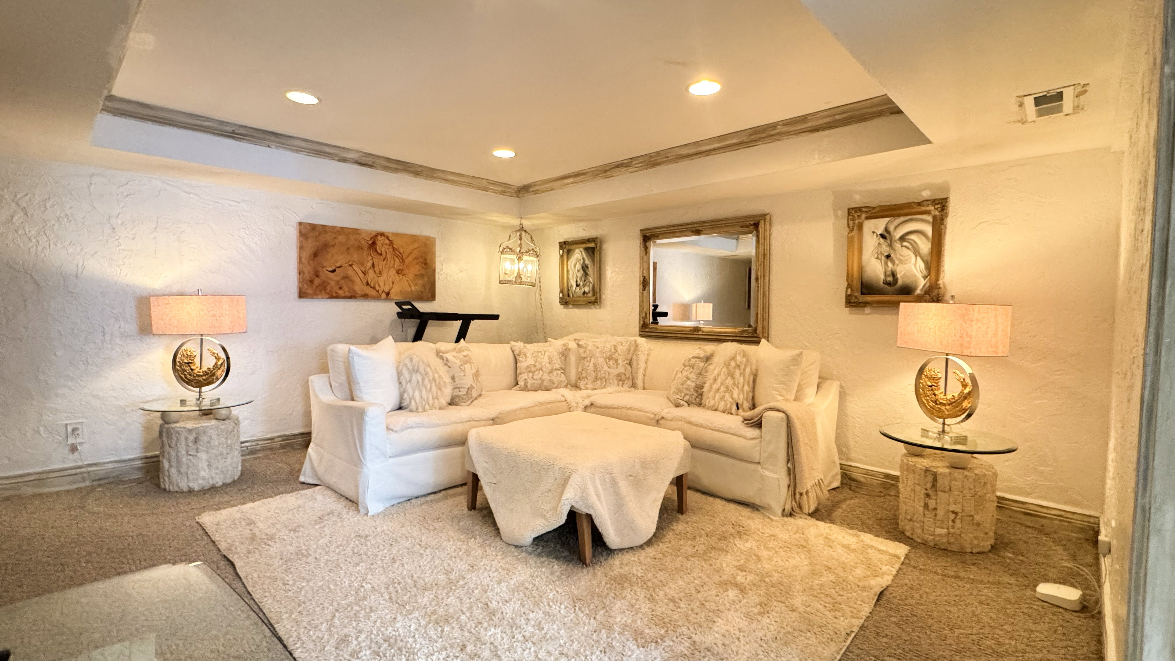 Recessed lighting illuminates a spacious room featuring textured white walls and contrasting ceiling details