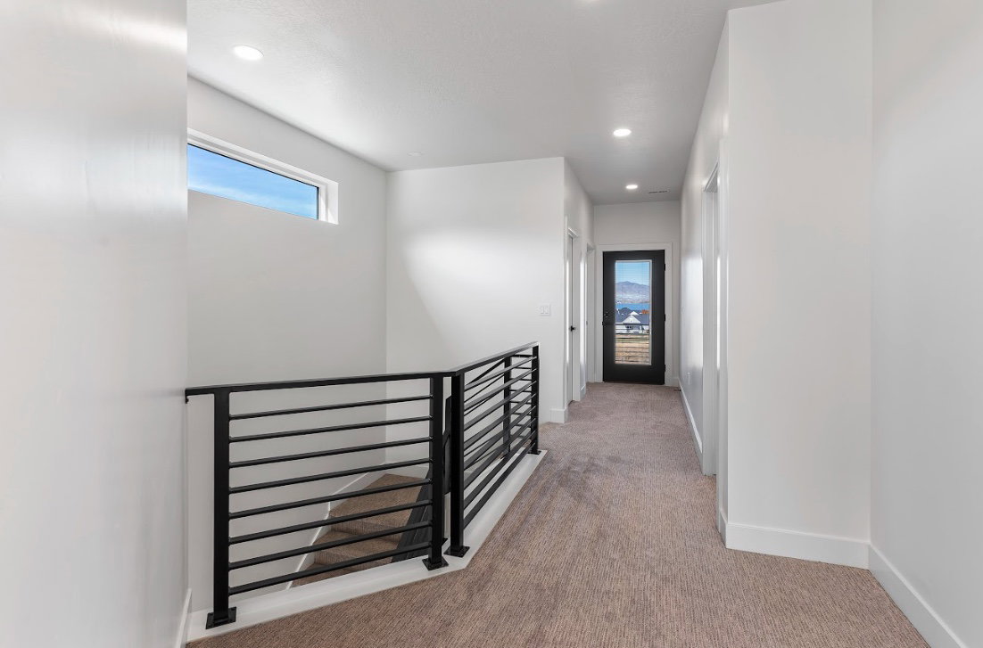 Upper-level hallway with modern black railing, recessed lighting, and a panoramic window