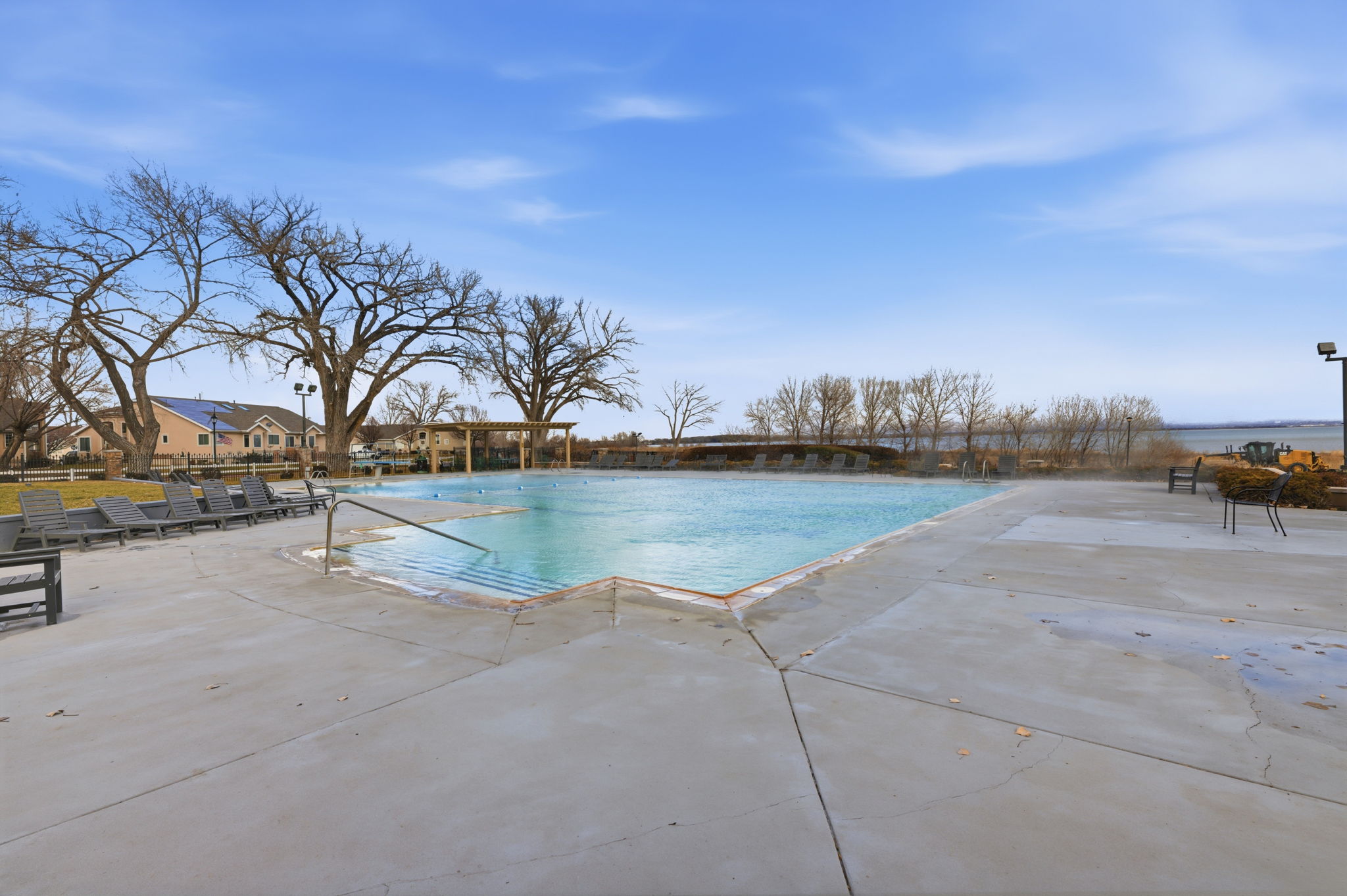 Expansive outdoor swimming pool with concrete decking, surrounded by mature trees, and featuring a background body of water