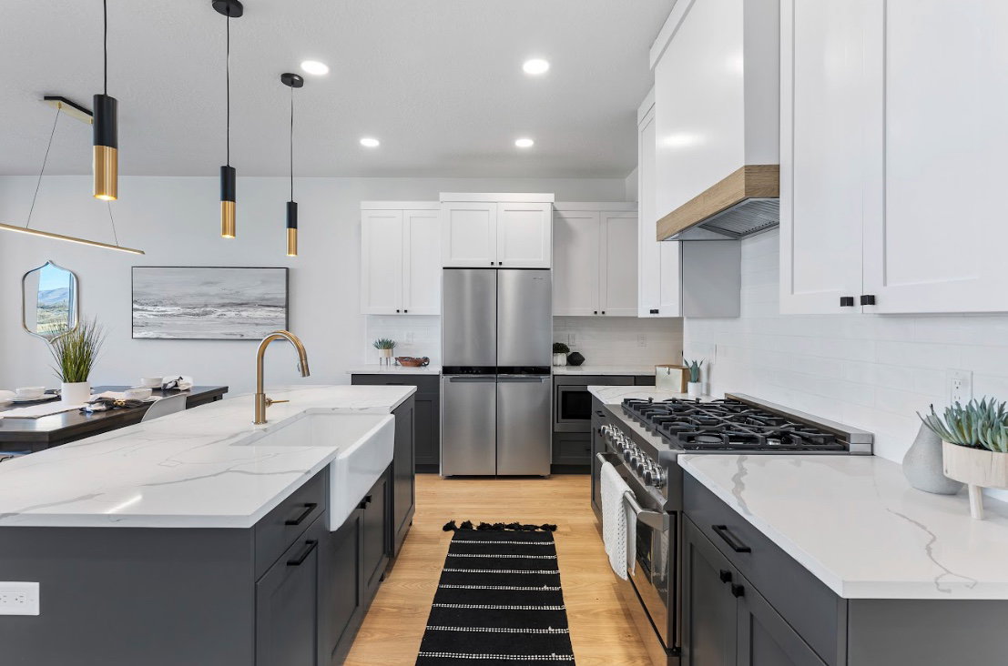 Kitchen featuring a large island with a farmhouse sink and brass faucet, stainless steel appliances, white subway tile backsplash, light wood-finish flooring, and pendant lighting