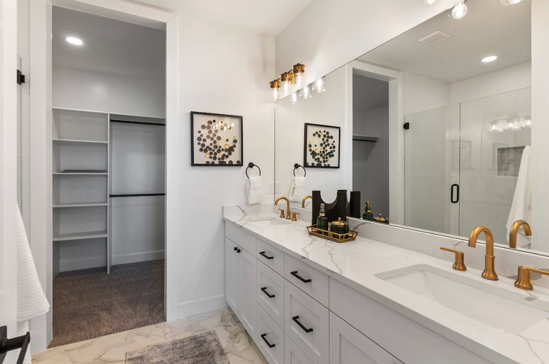 Bathroom featuring a dual vanity with white cabinetry, white countertops, and gold-finish fixtures