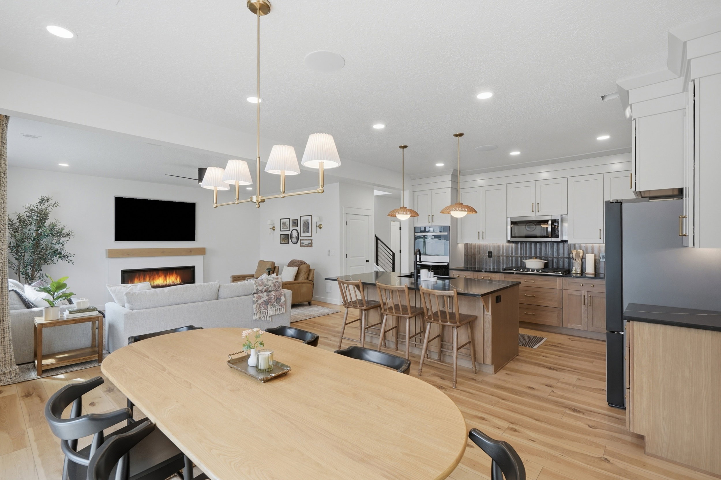 Open-concept living space featuring wood-finish flooring, a contemporary kitchen with an island, sleek black appliances, and white upper cabinetry