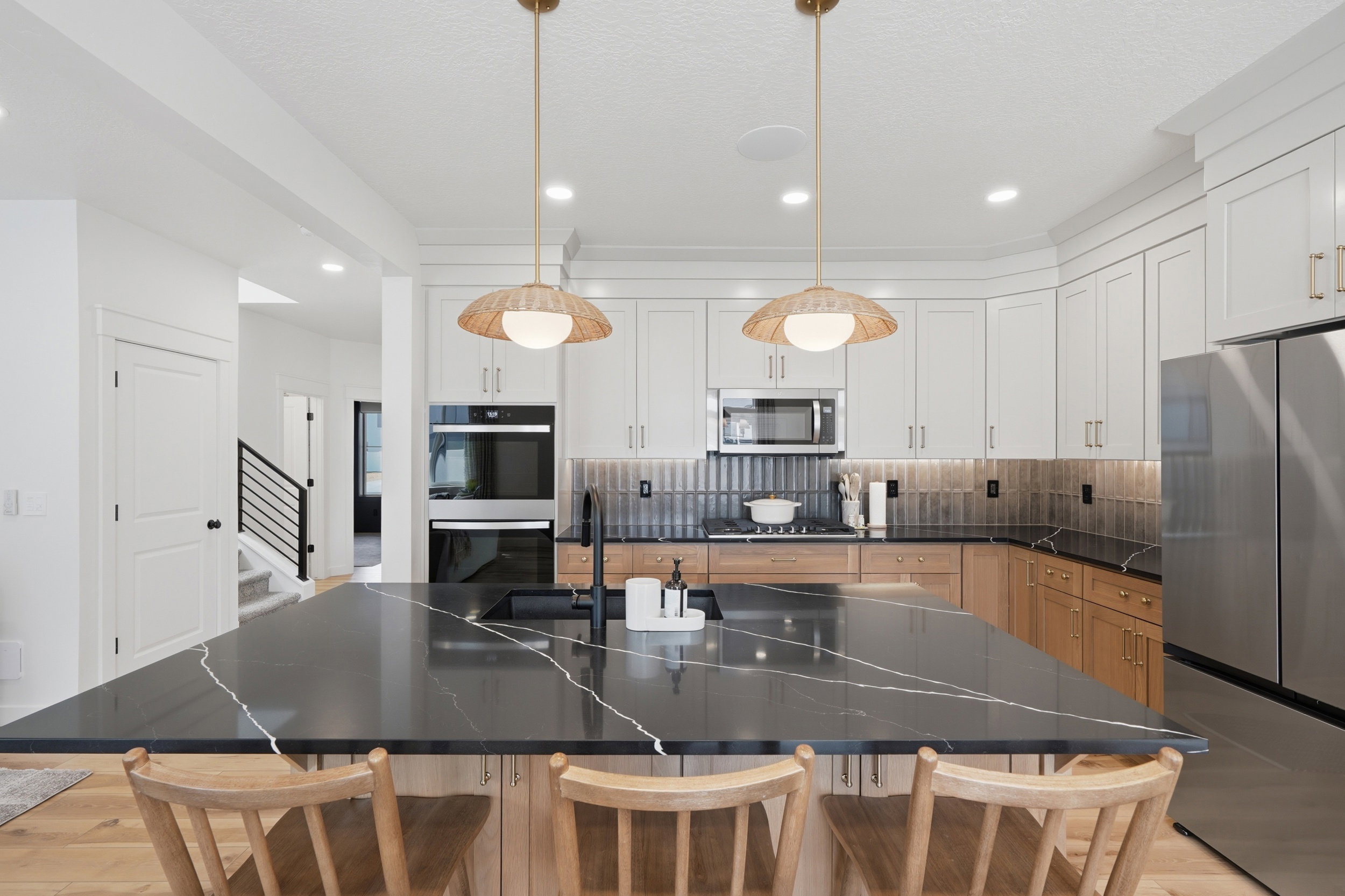 Spacious kitchen featuring a large island with a dark countertop, white upper cabinetry, natural wood lower cabinetry, stainless steel appliances, and distinctive pendant lighting
