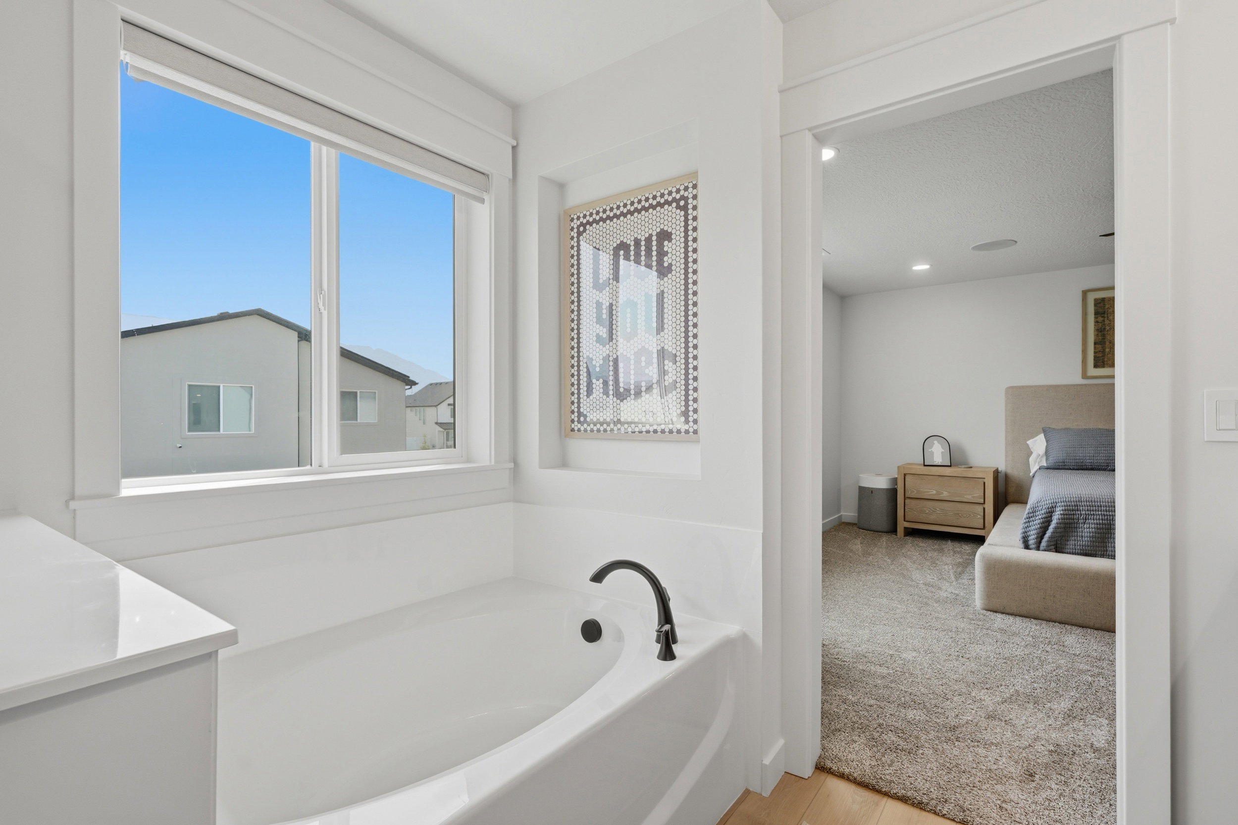 Soaking tub with a matte black faucet, surrounded by white trim and a white countertop