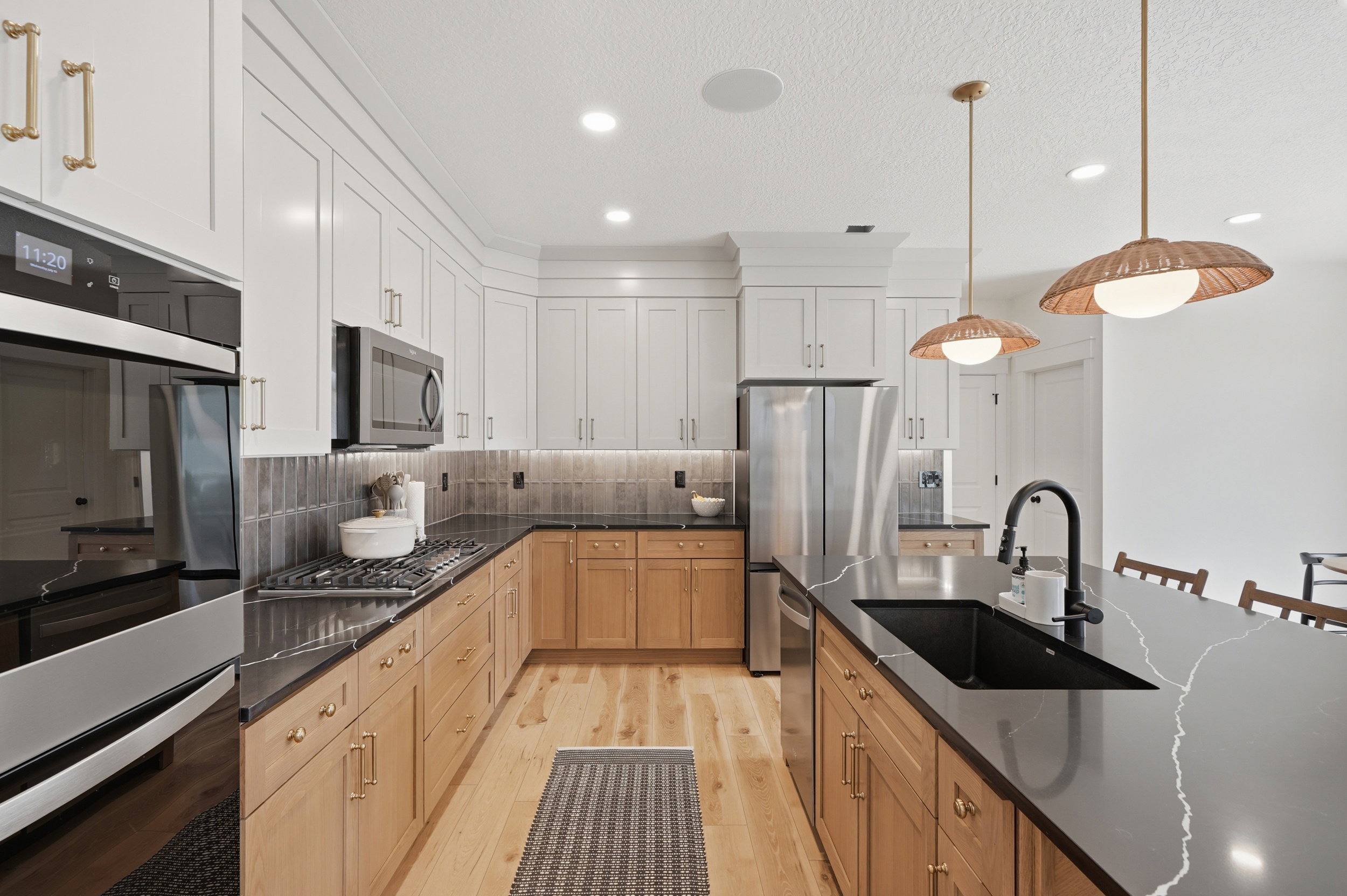 Modern kitchen featuring a large island with an integrated sink, dual-toned cabinetry, stainless steel appliances, dark countertops, and wood-finish flooring