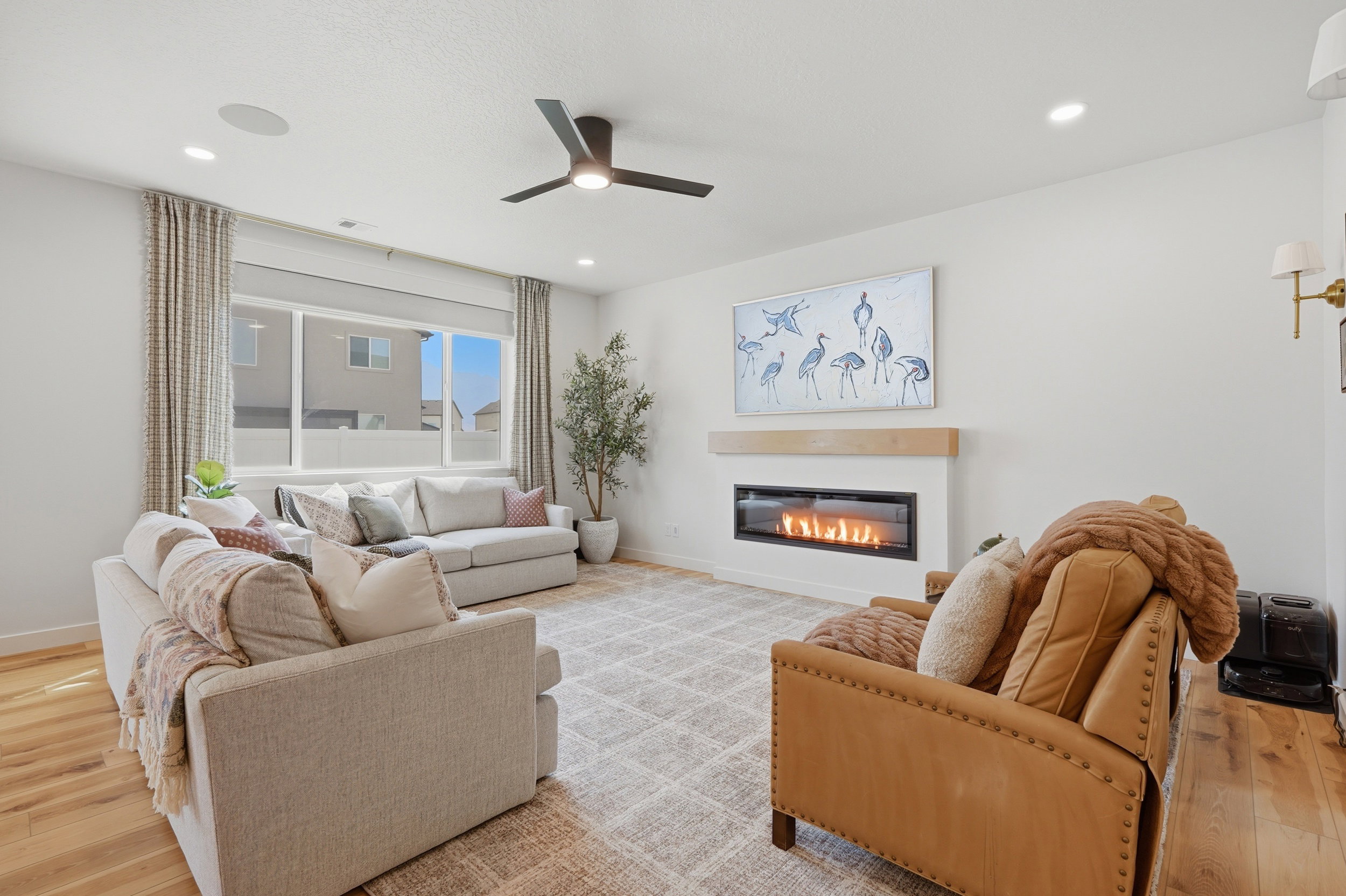 Spacious living area featuring a linear gas fireplace with a wood mantle, large windows with natural light, recessed lighting, and a ceiling fan
