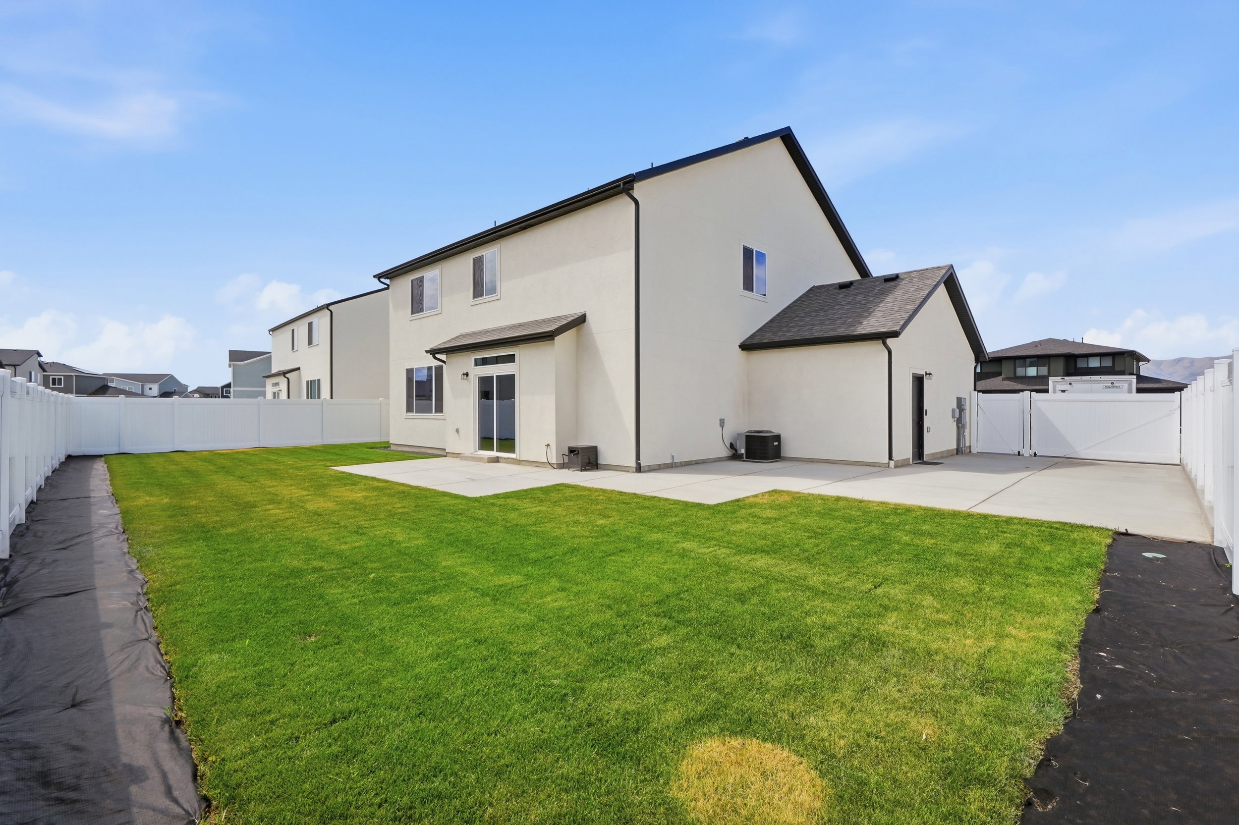 Spacious backyard with a large concrete patio, a verdant lawn, and a white vinyl privacy fence