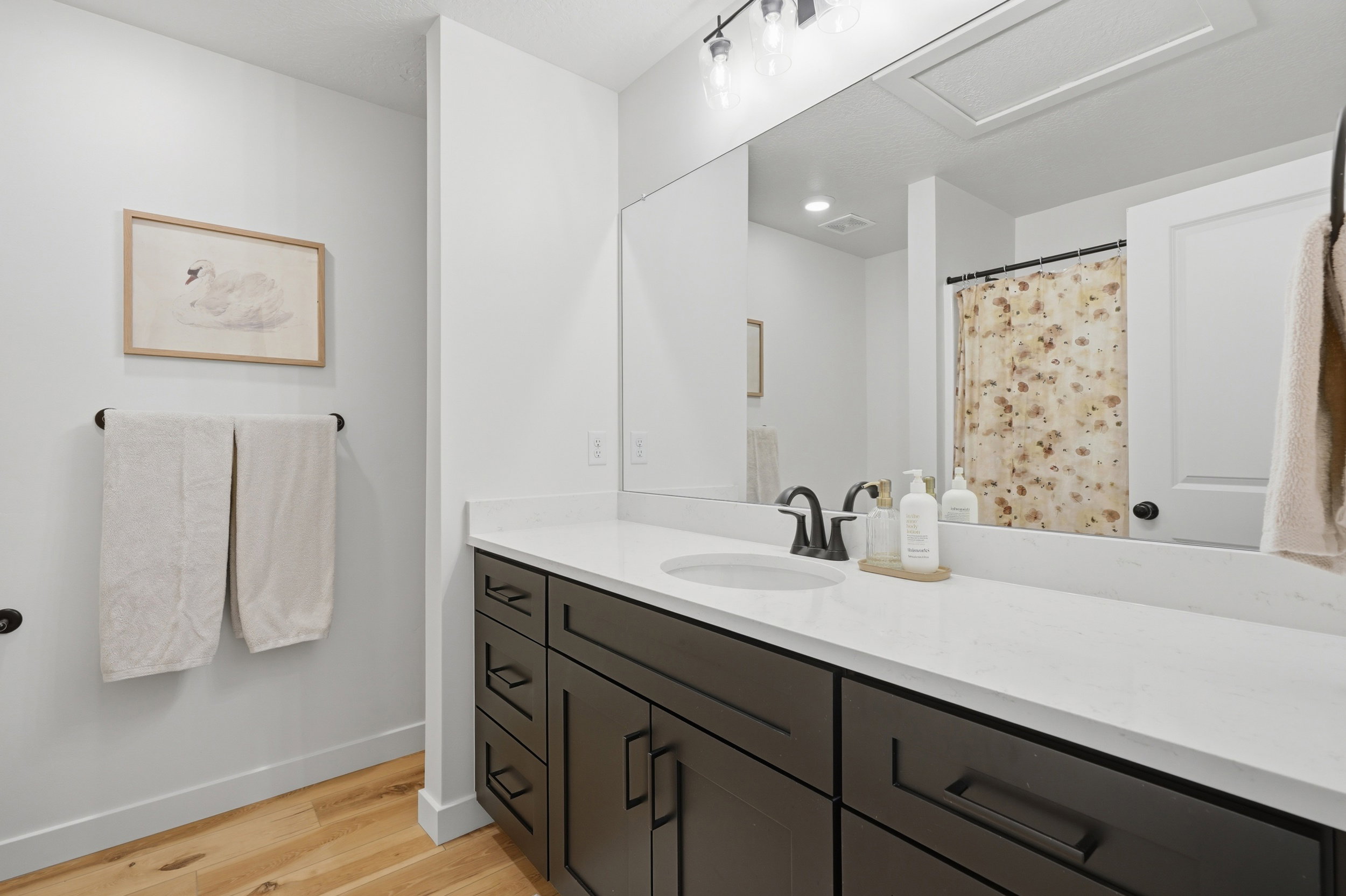 Bathroom featuring a dark wood-finish vanity with ample storage, a white countertop with integrated sink, and a large wall-mounted mirror