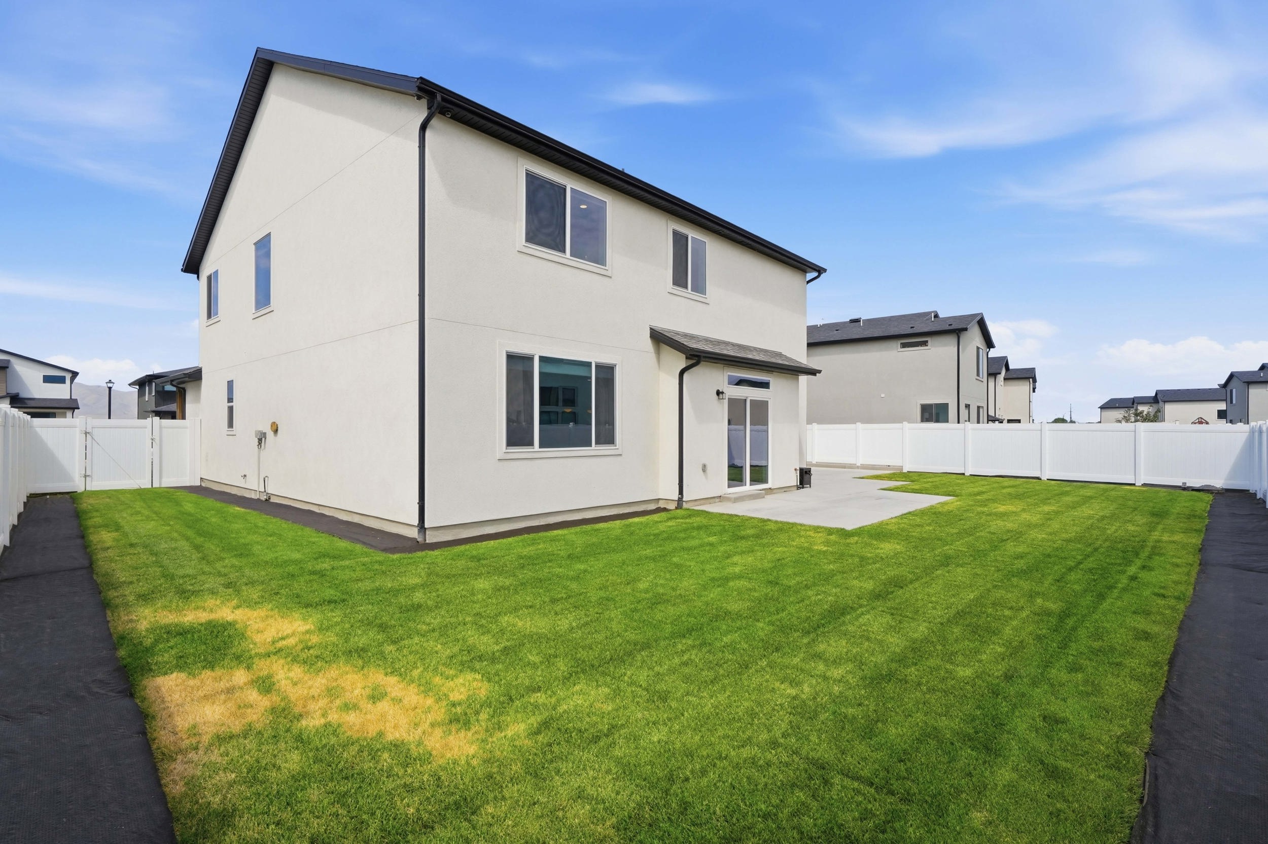 Spacious backyard featuring a large green lawn, a concrete patio, and a white privacy fence